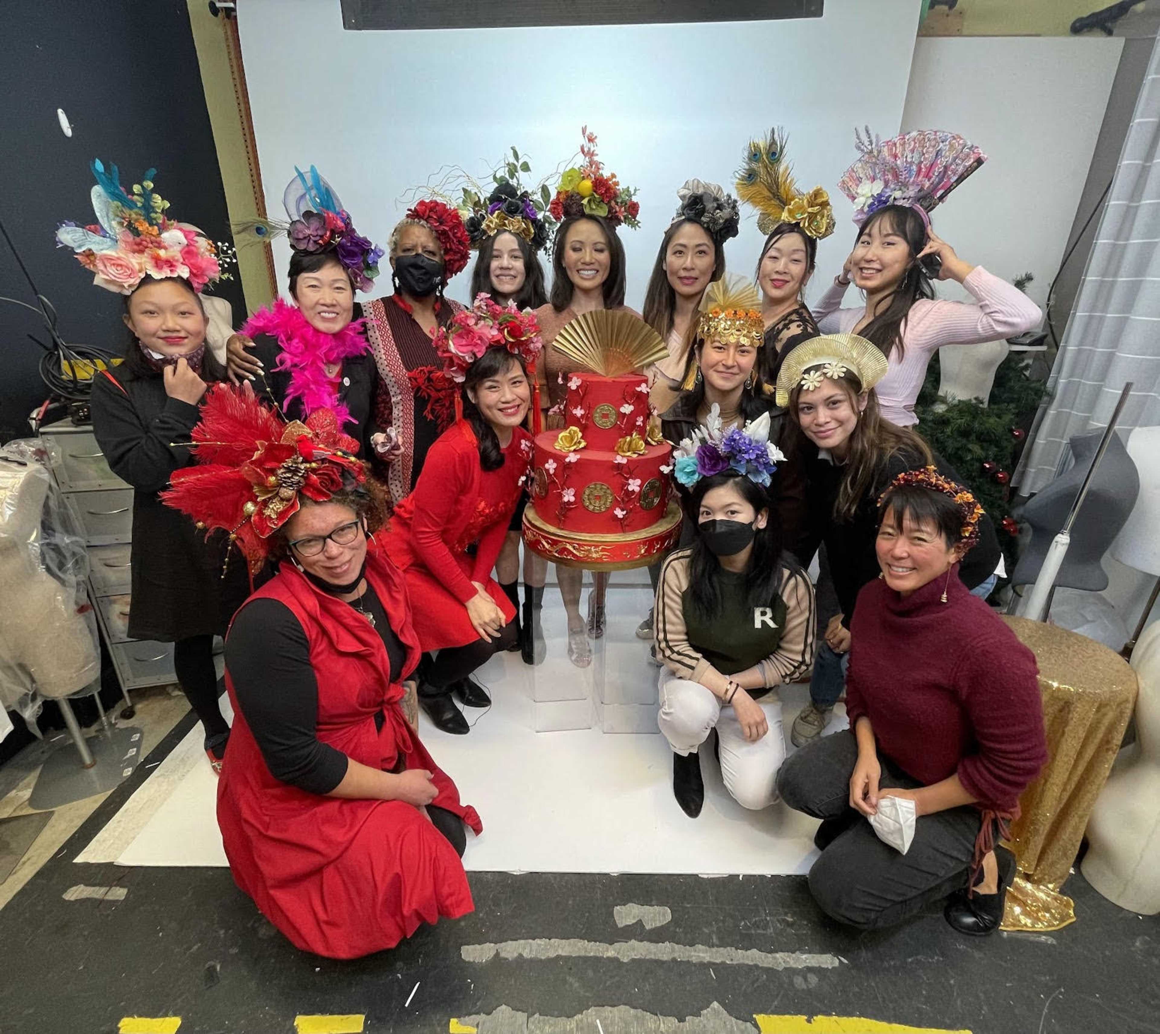 A diverse group of people poses together around a large, decorated cake in a festive setting.