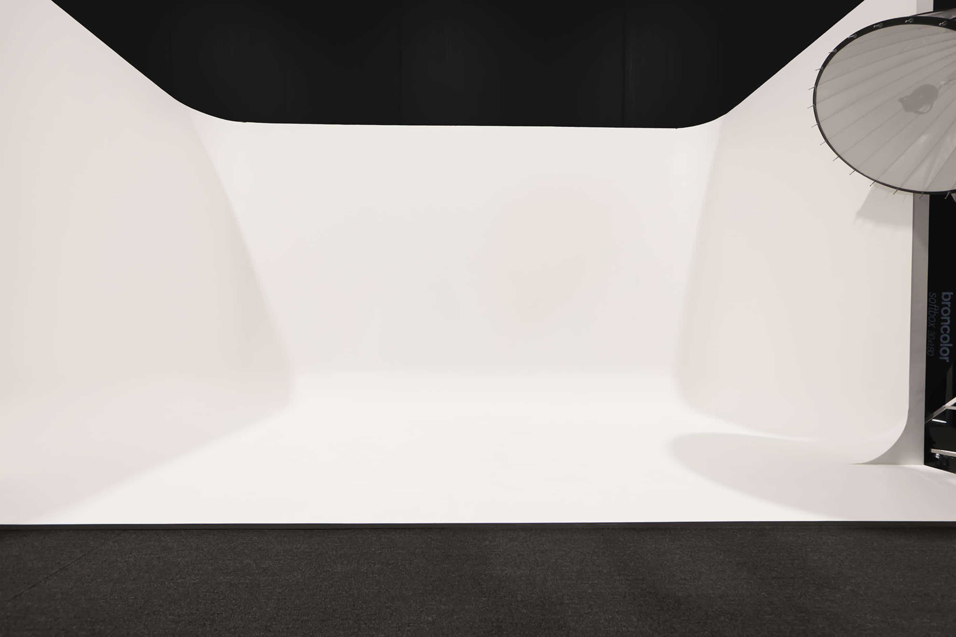 A well-lit photo studio with a seamless white backdrop and a large circular softbox light.
