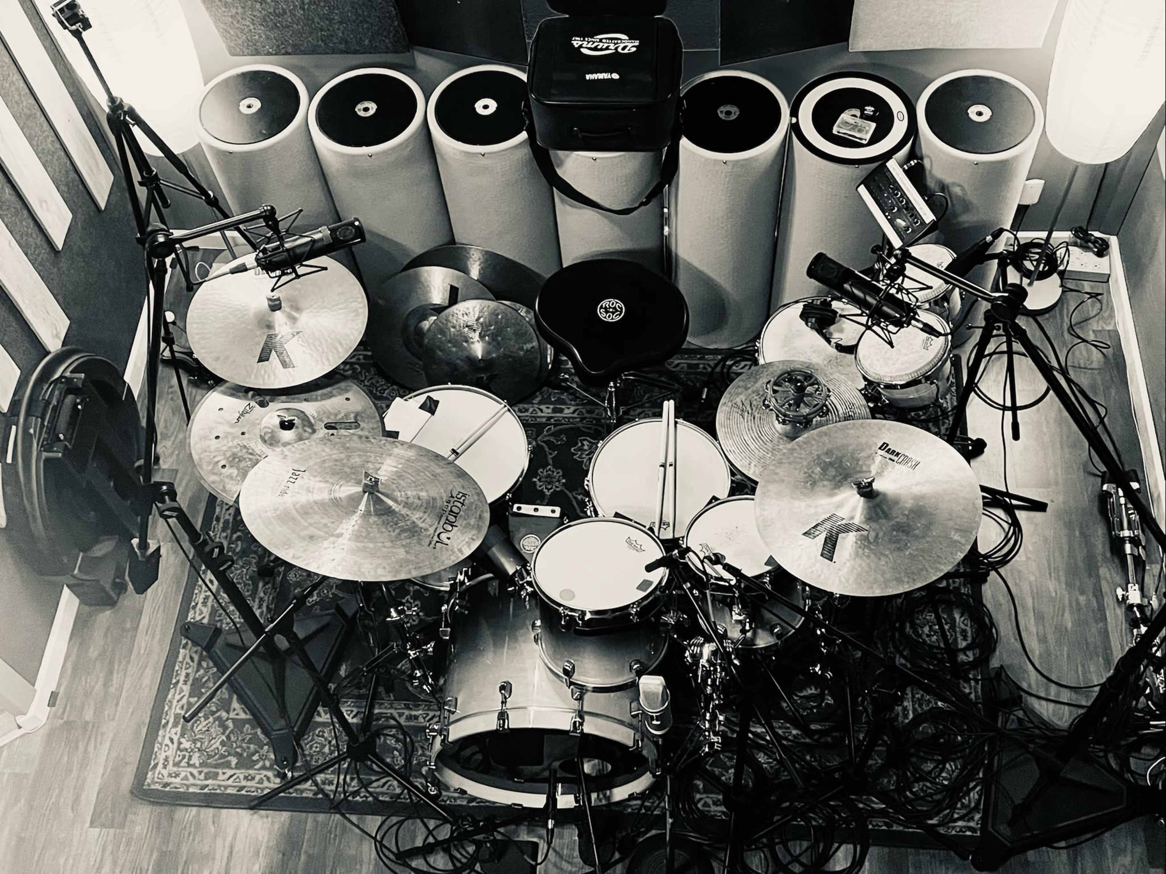 An overhead view of a drum set surrounded by sound equipment and cylindrical objects in a recording studio.