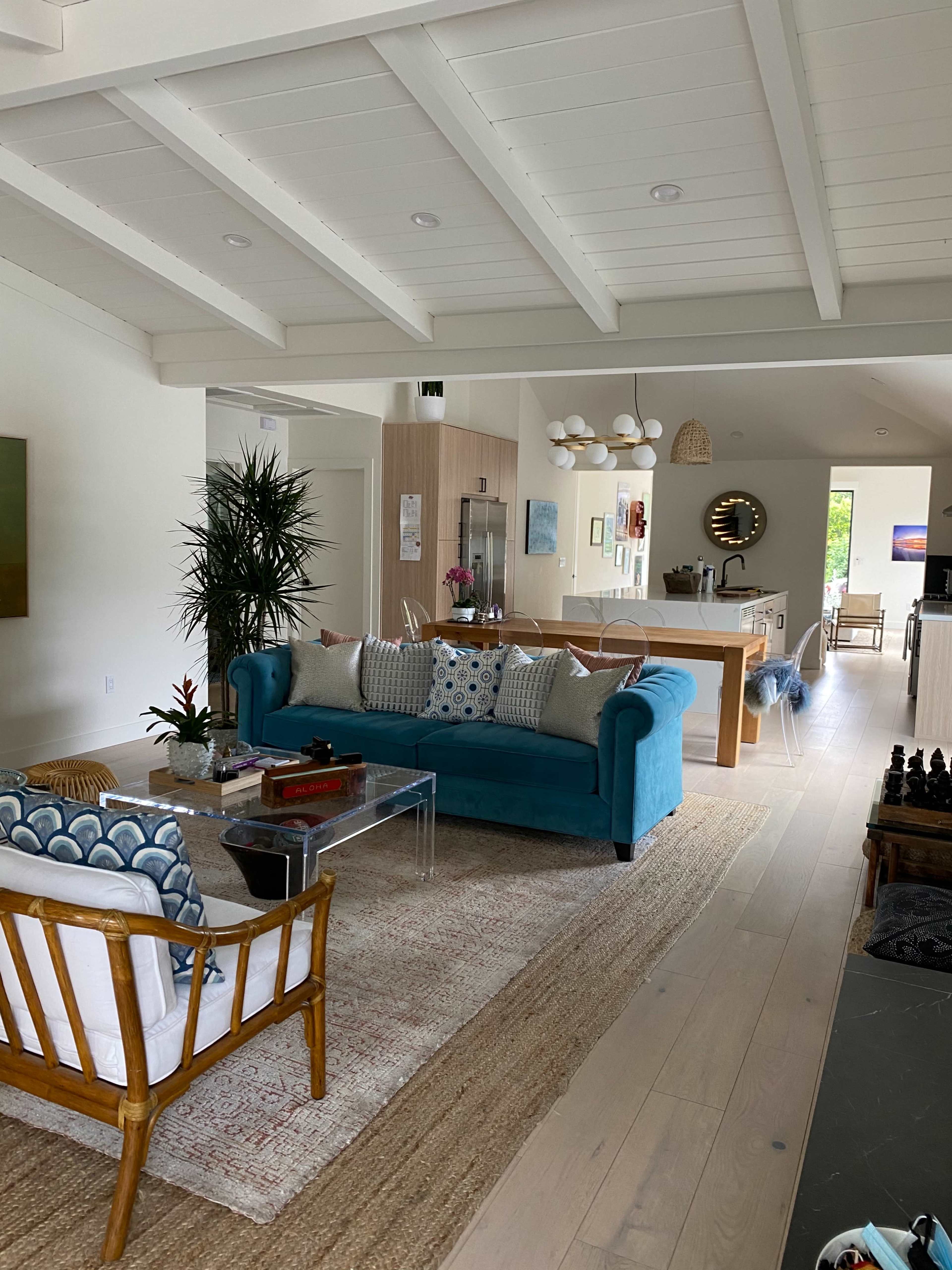 A spacious living area with a turquoise sofa, a glass coffee table, and an adjacent kitchen visible in the background.