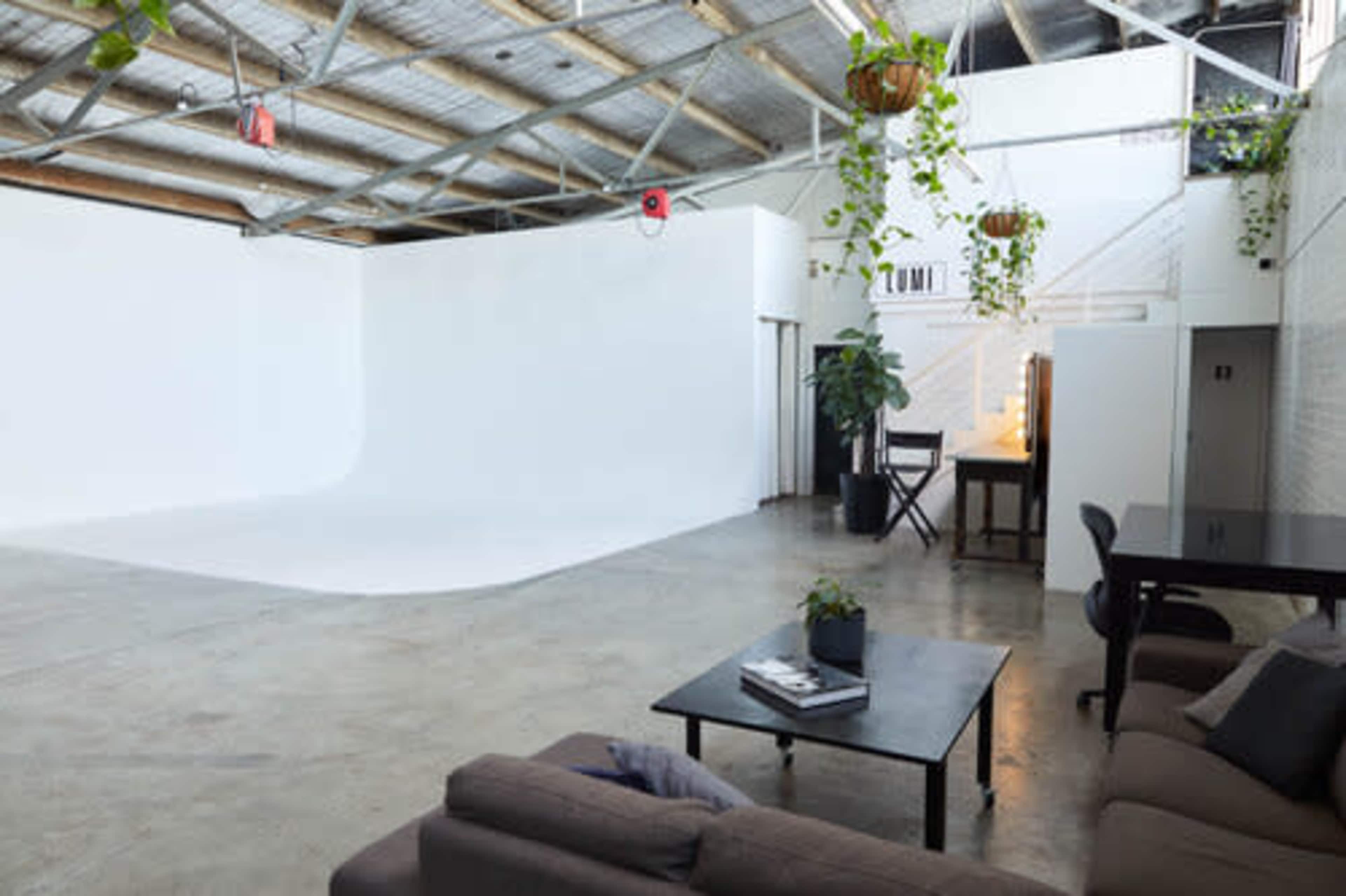 A spacious studio with a white backdrop, concrete flooring, and a seating area with a sofa and a coffee table.
