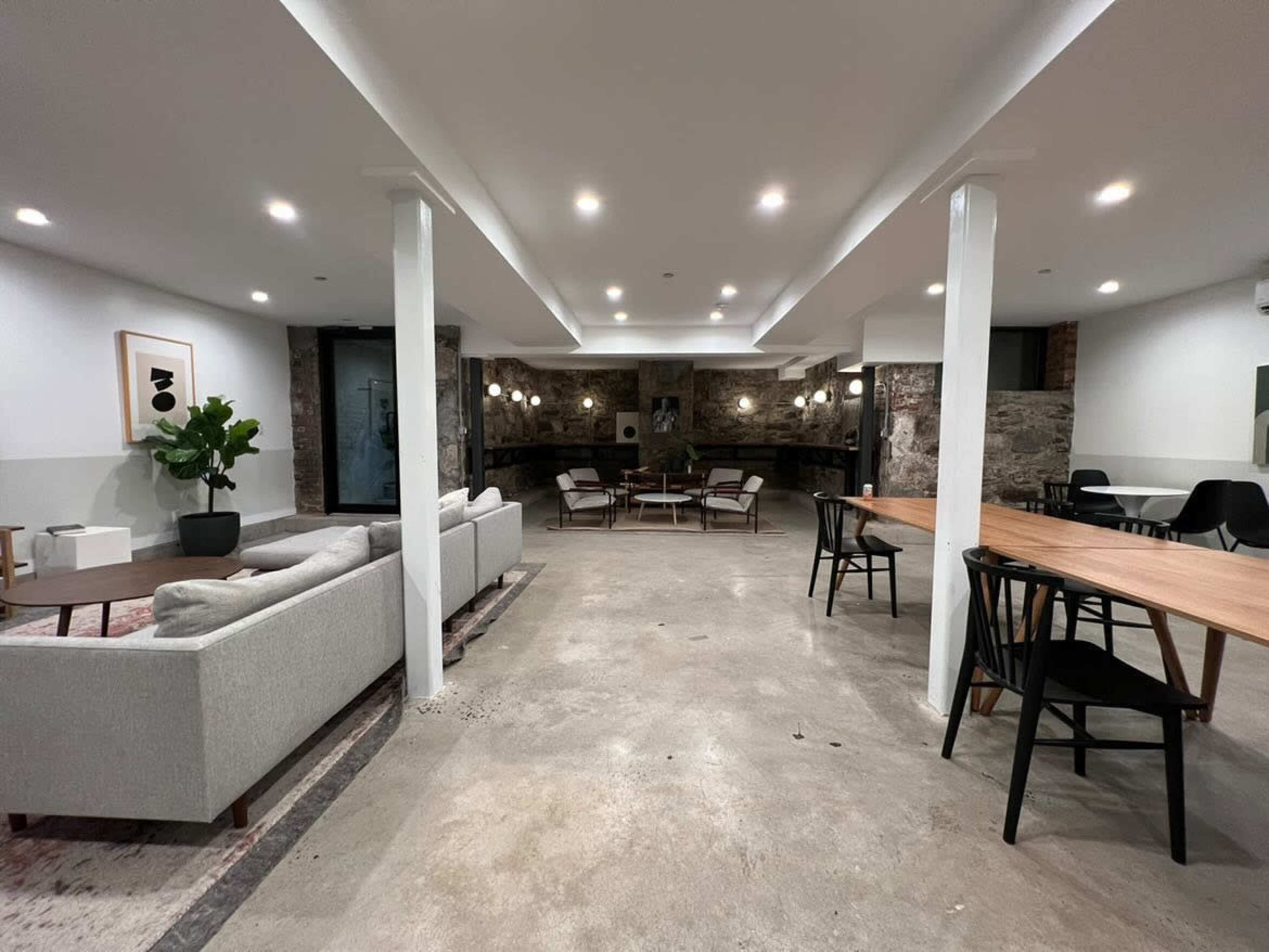 A spacious, modern lounge area with a combination of seating options, including a sofa, chairs, and dining tables, set against a backdrop of stone walls and soft lighting.