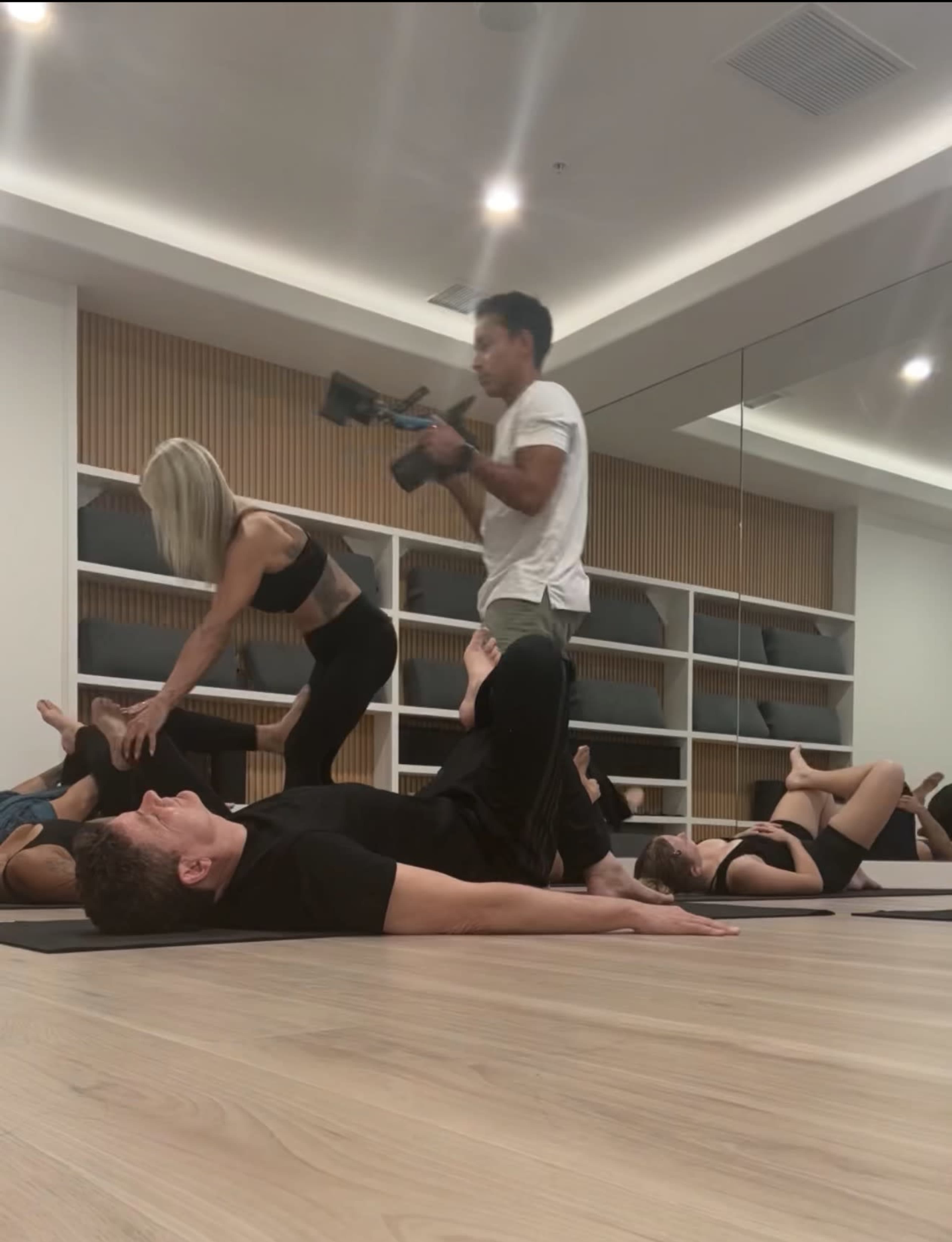 A group of people is participating in a yoga or fitness session while one person films the activity.