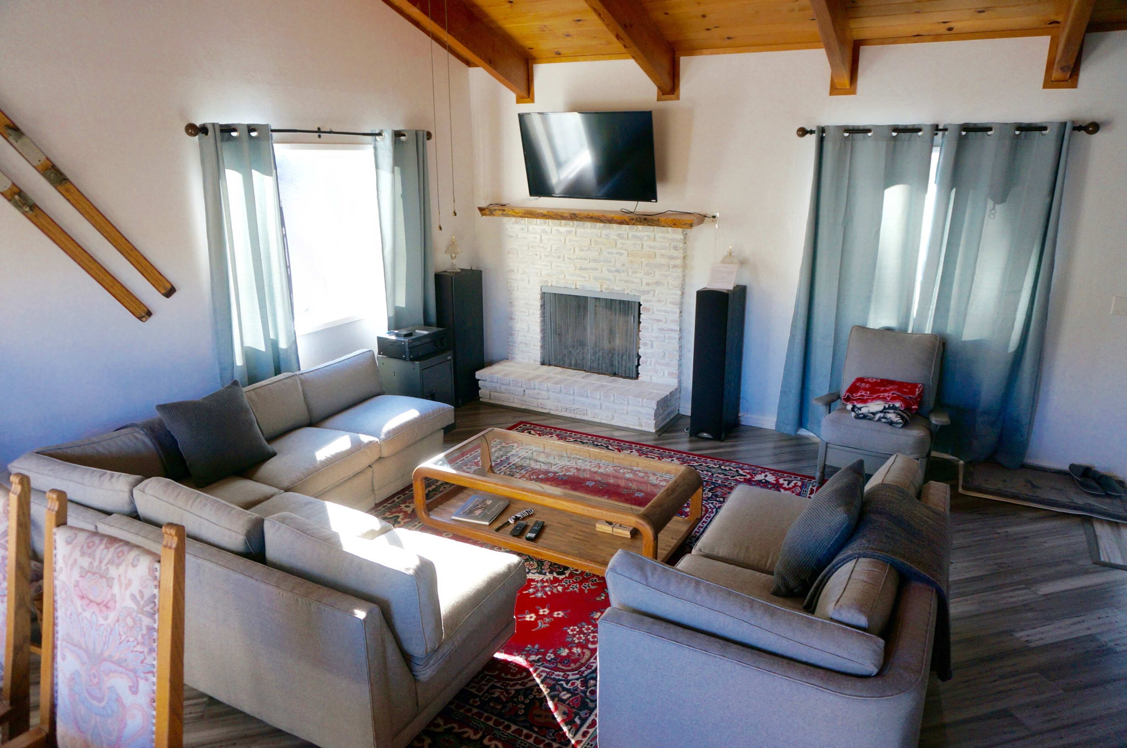 The image shows a living room with a fireplace, two large couches arranged in an L-shape, and a coffee table on a patterned rug.