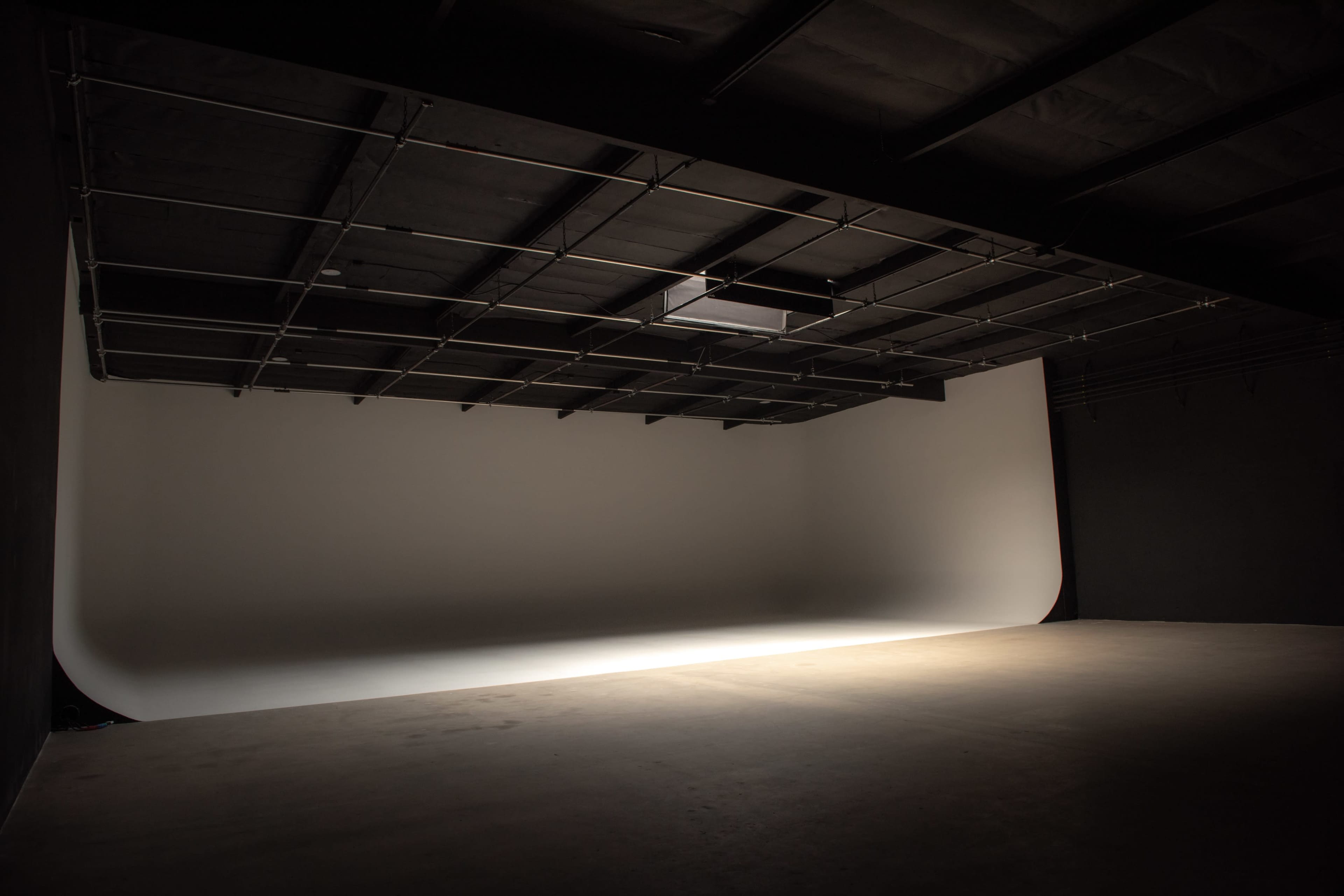 A large, empty studio space with a seamless white backdrop and a dimly lit concrete floor.