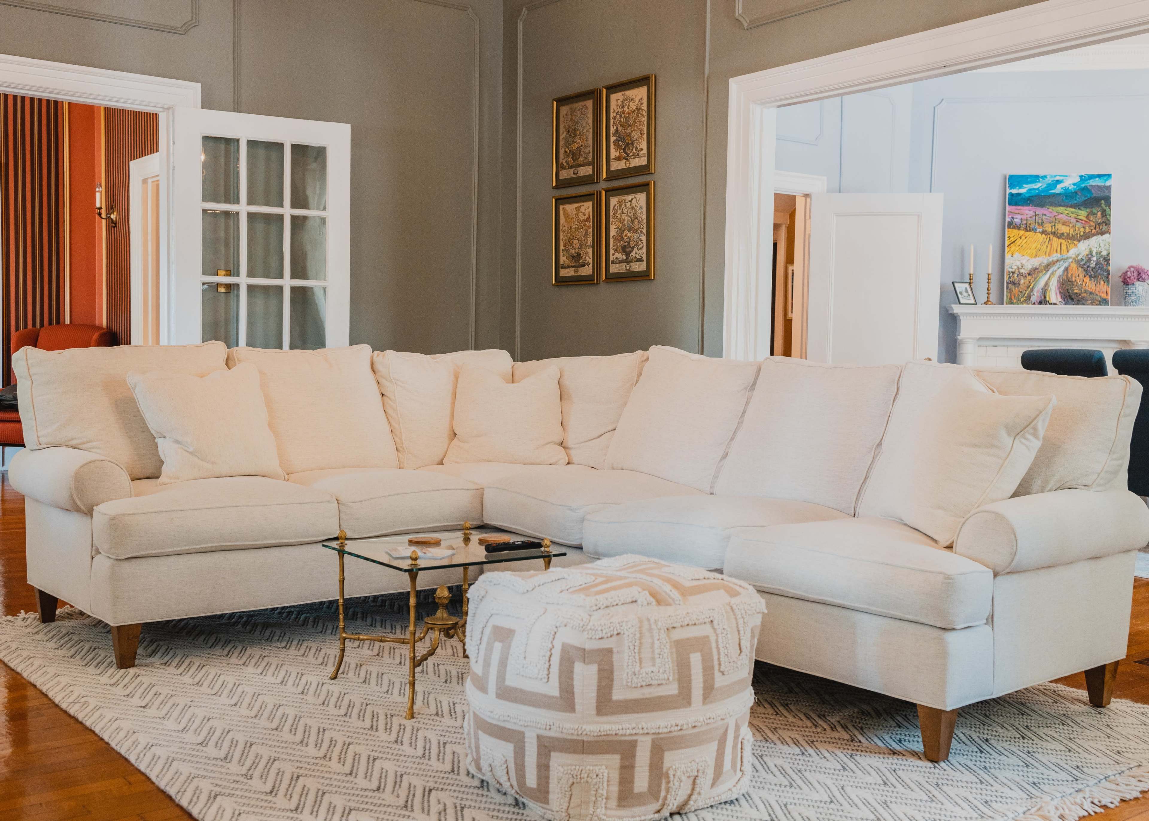 A light-colored sectional sofa with several cushions sits on a patterned area rug in a room with gray walls and multiple doorways.