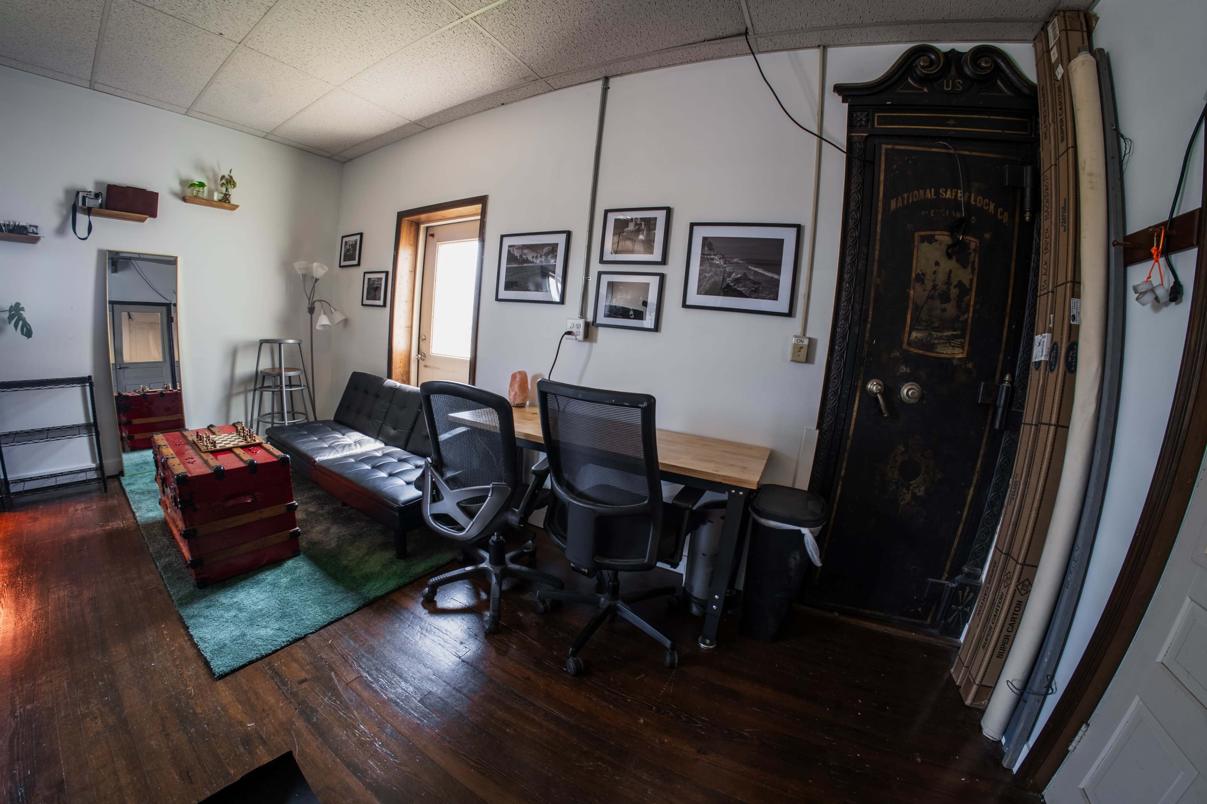 The image shows a small office space with a mix of furniture, including a couch, a desk with chairs, and a door with an old-fashioned design.