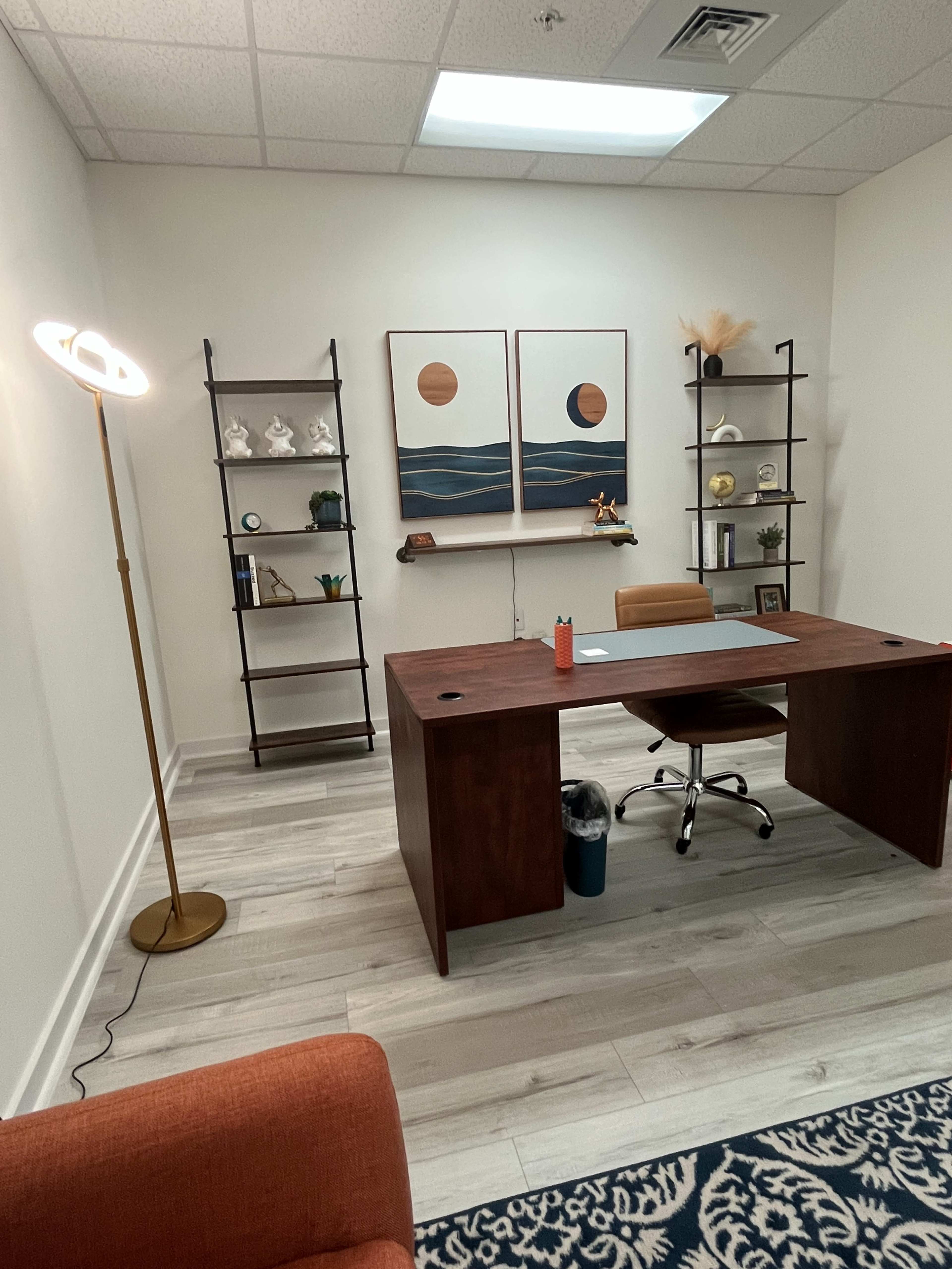 A modern office space featuring a wooden desk, a chair, and decorative shelves with plants and artwork on the walls.
