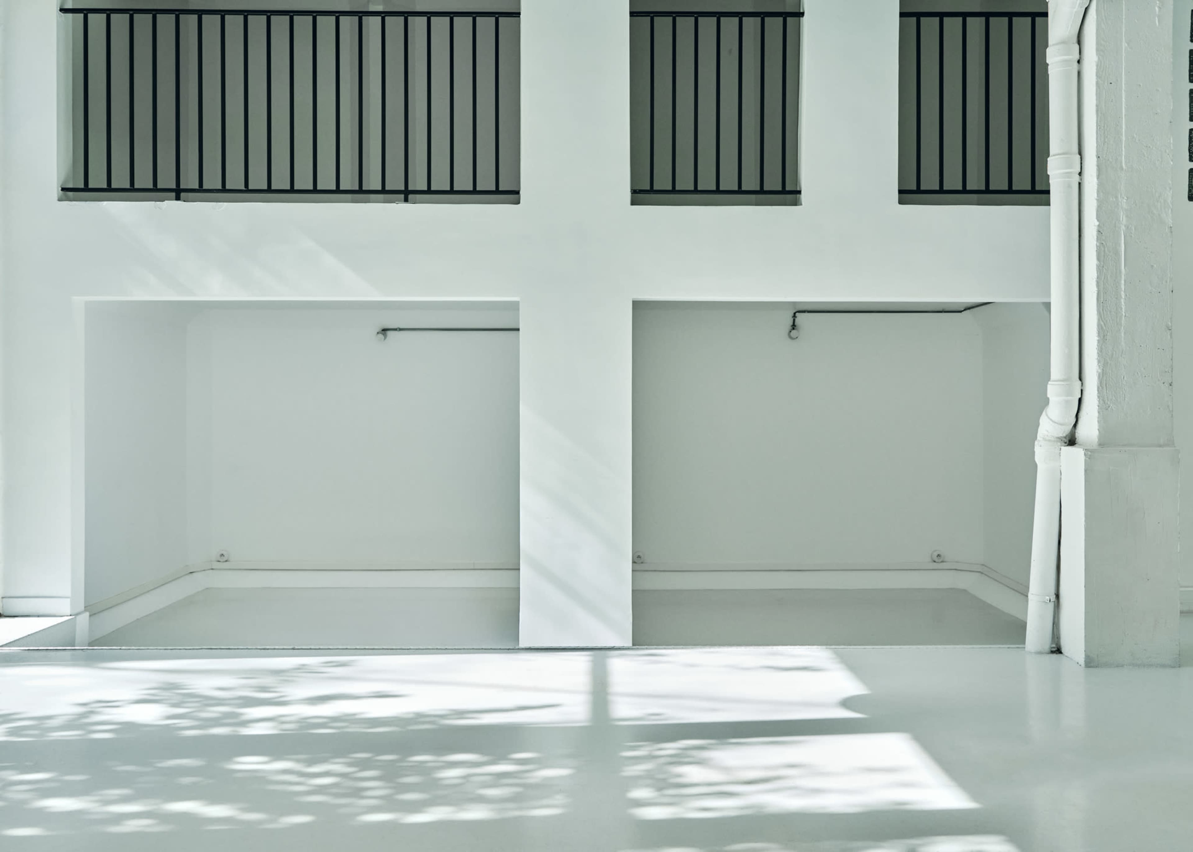 The image shows a minimalist interior space with white walls, a polished floor, and two recessed areas beneath balconies.