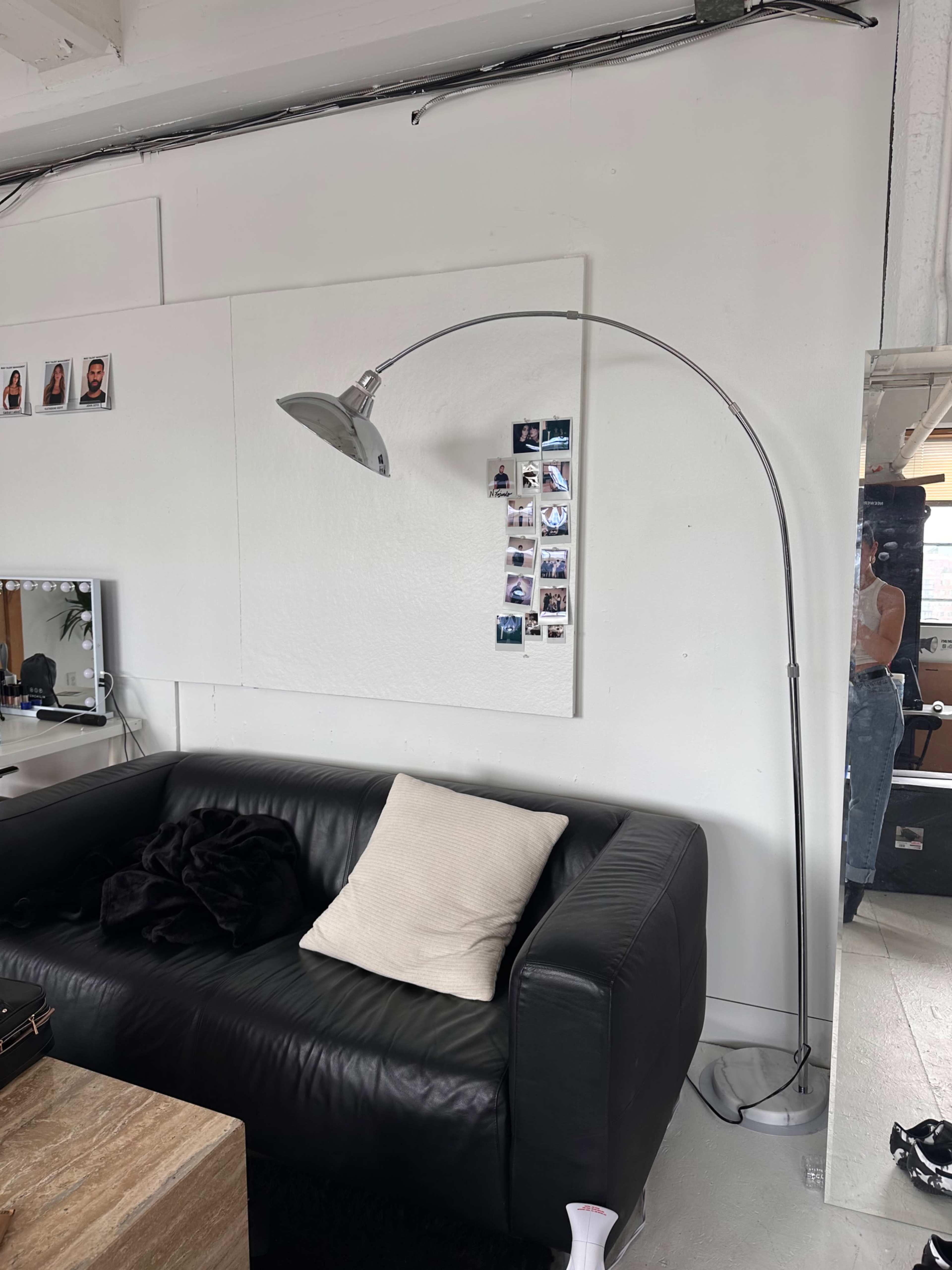The image shows a modern room with a black leather sofa, an arching floor lamp, and a collage of photos pinned to the wall.