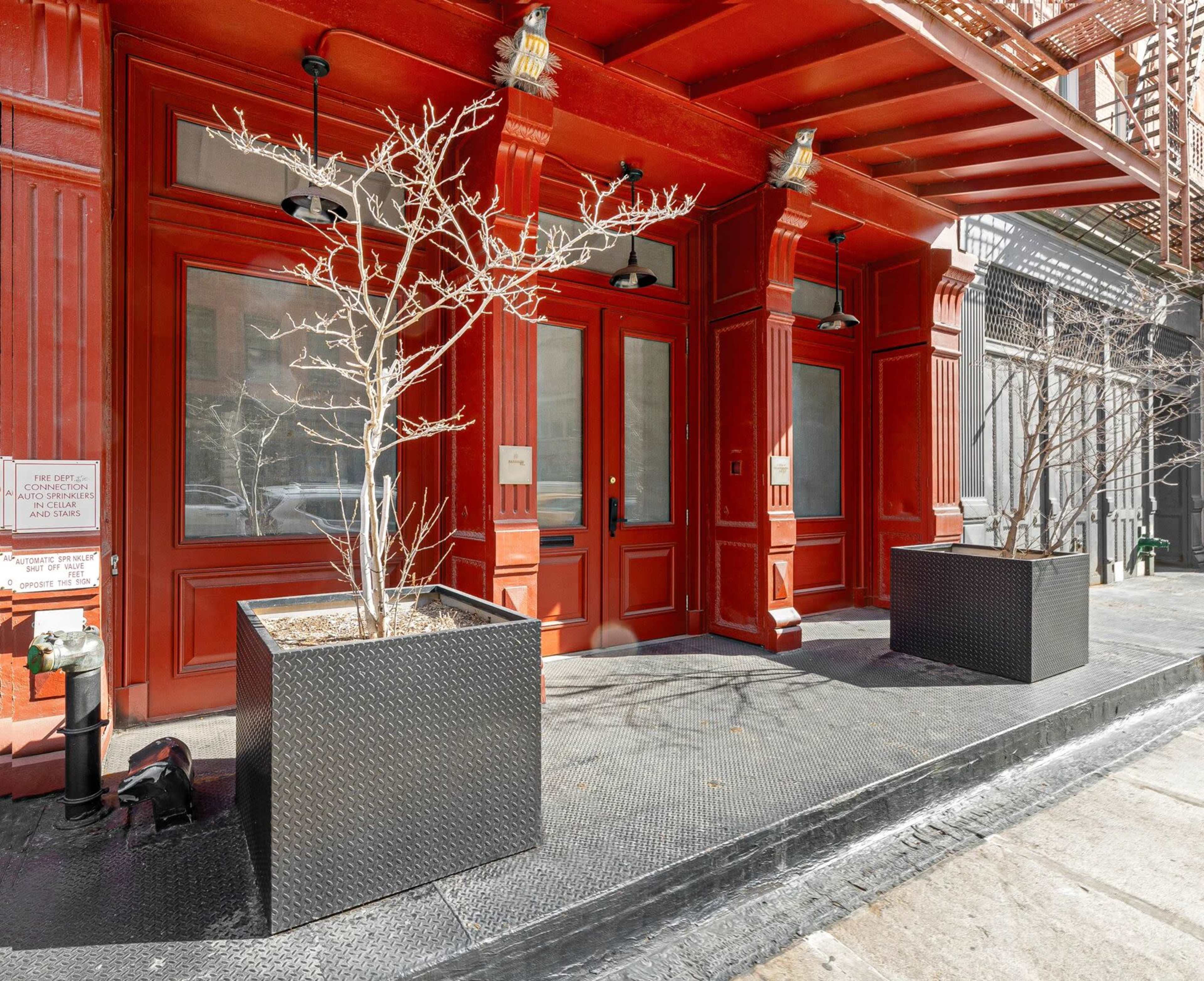The image shows the exterior of a building with a bright red facade and two planters containing bare trees on the sidewalk.