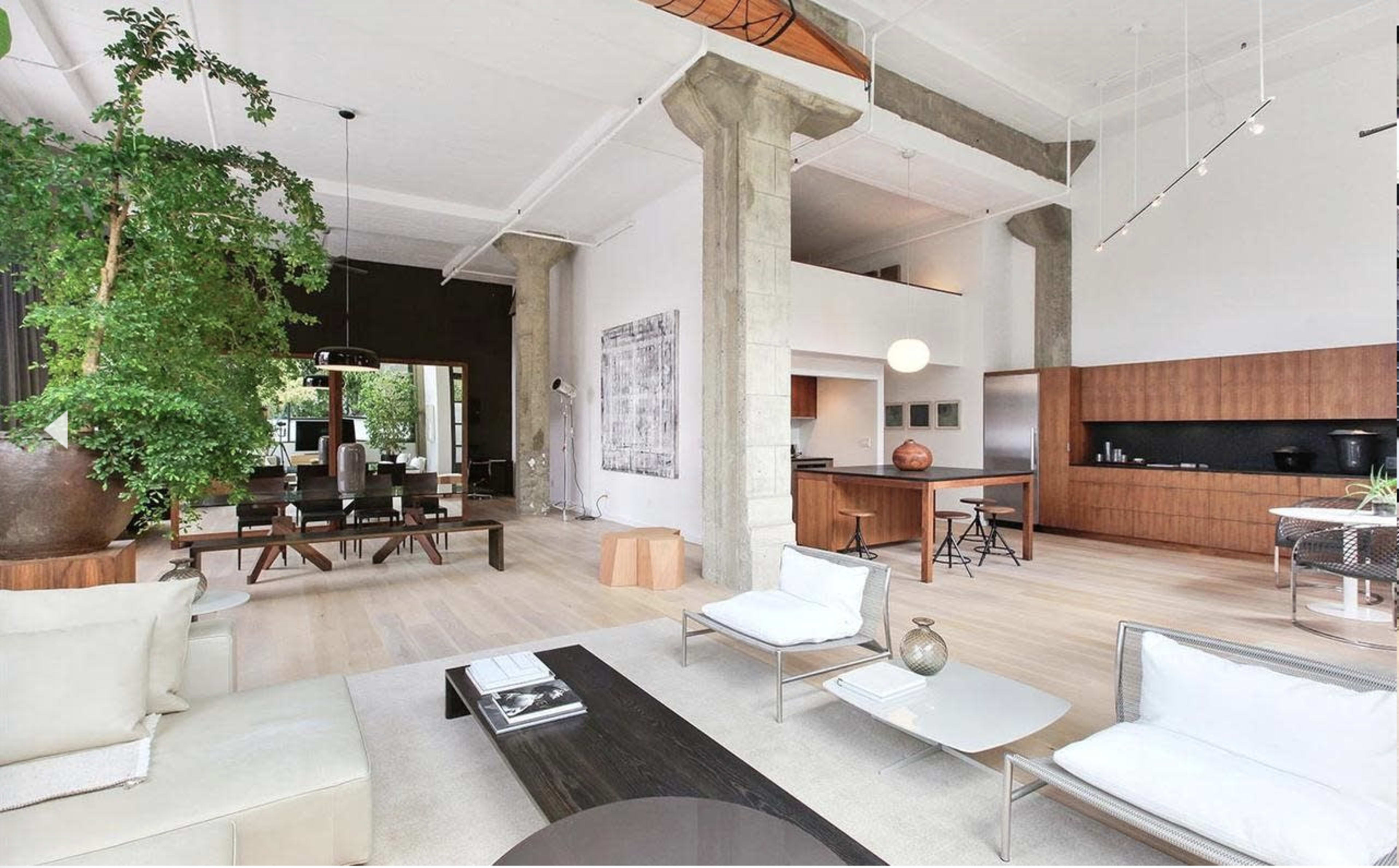 A spacious modern living area with an open floor plan, featuring a kitchen, dining area, and a lounge space, illuminated by natural light.