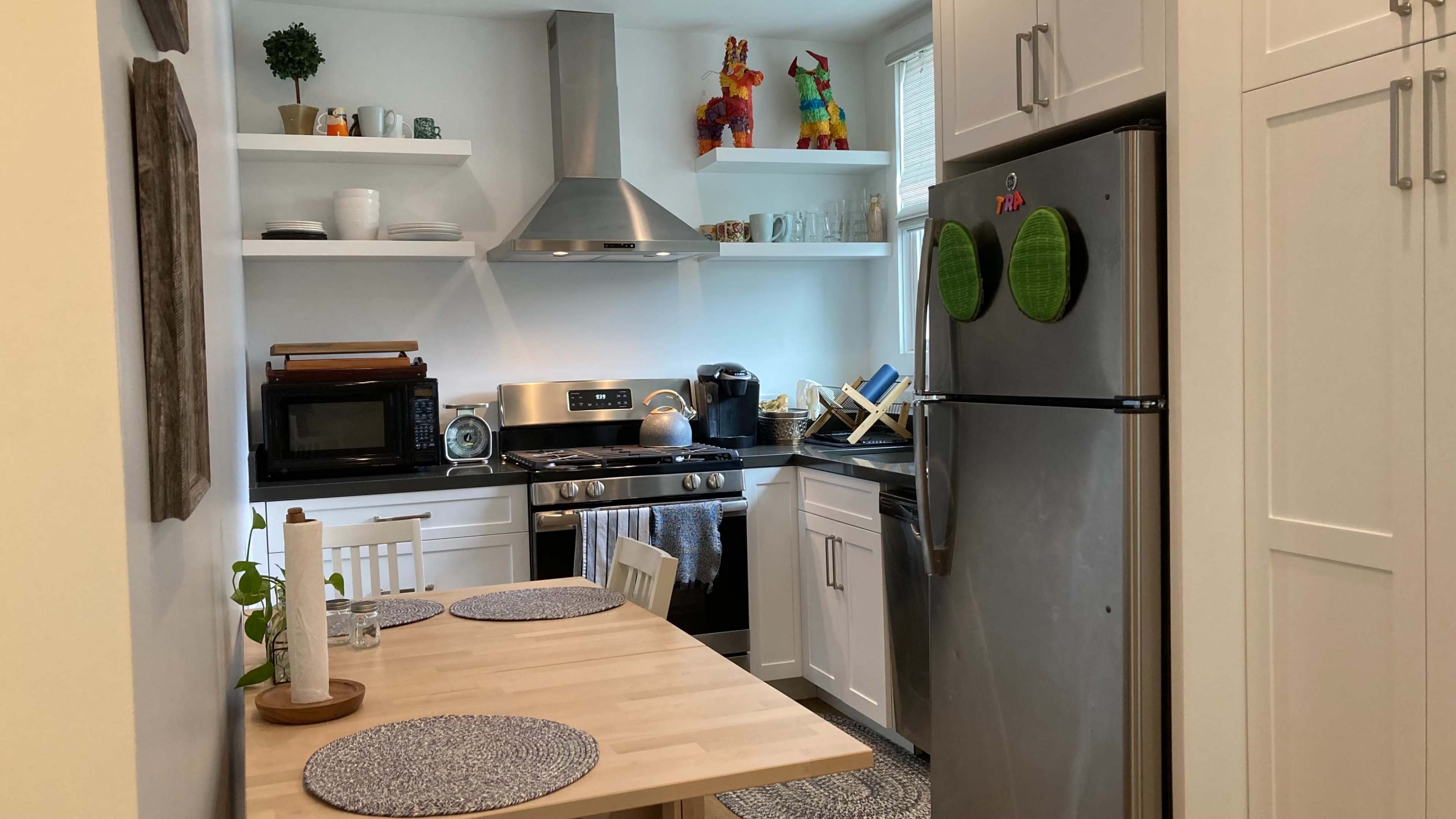 A compact kitchen features stainless steel appliances, white cabinets, and a dining table set for two.