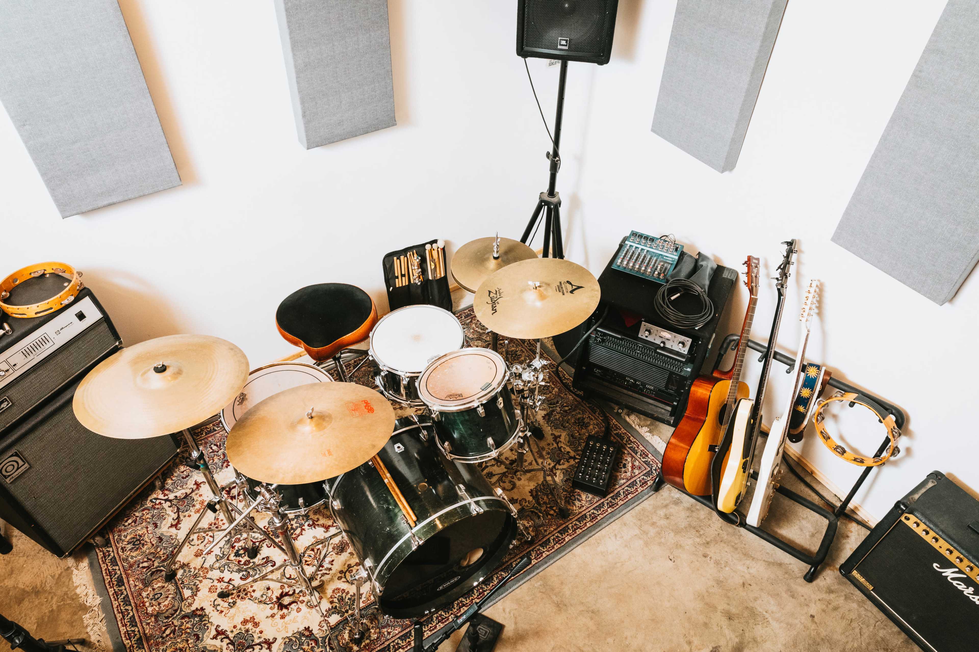 A music practice space featuring a drum set, amplifiers, guitars, and various percussion instruments arranged on a rug.