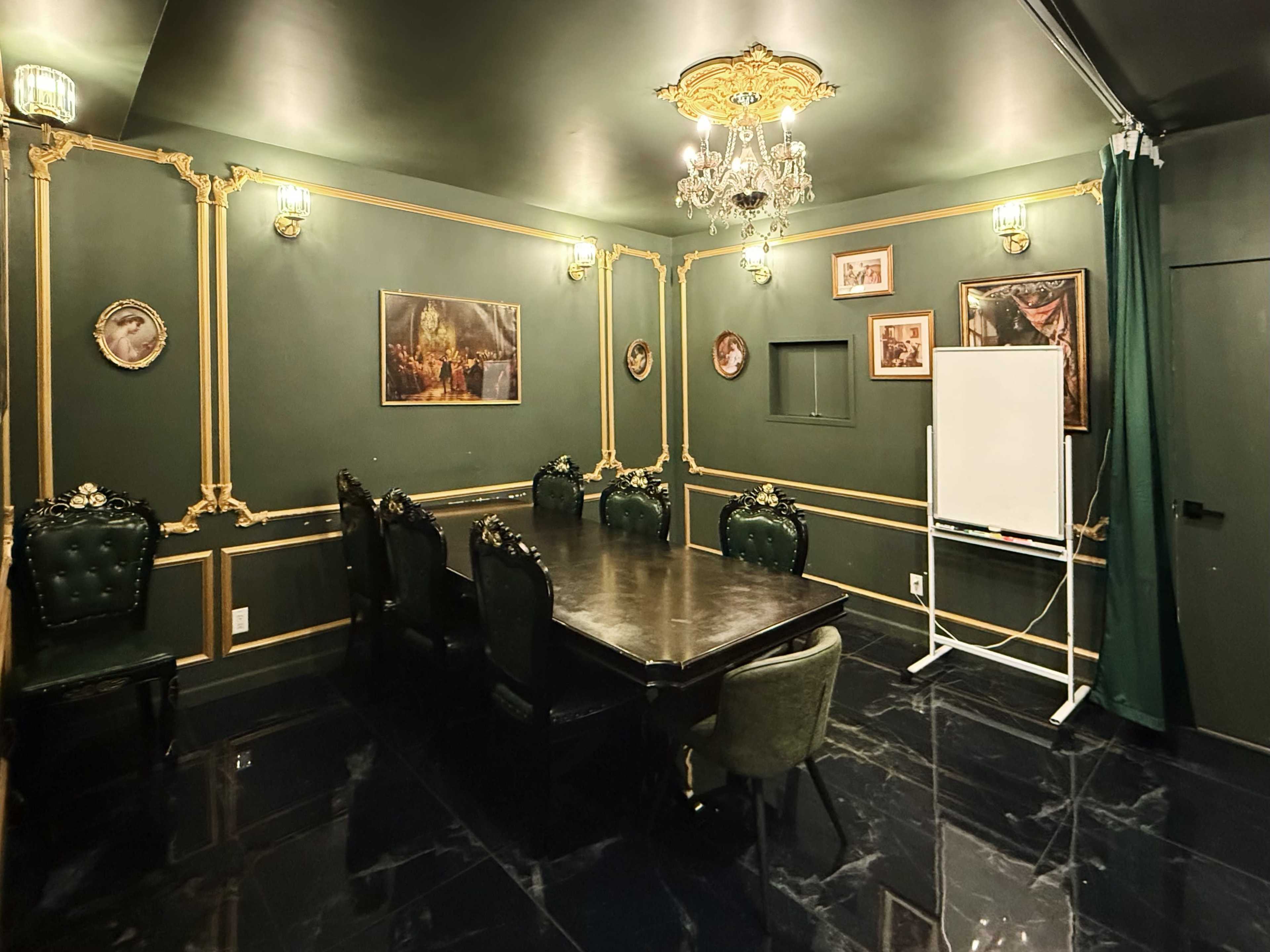 The image shows an elegant meeting room with dark walls, ornate gold detailing, a large table surrounded by high-backed chairs, and framed artwork on the walls.