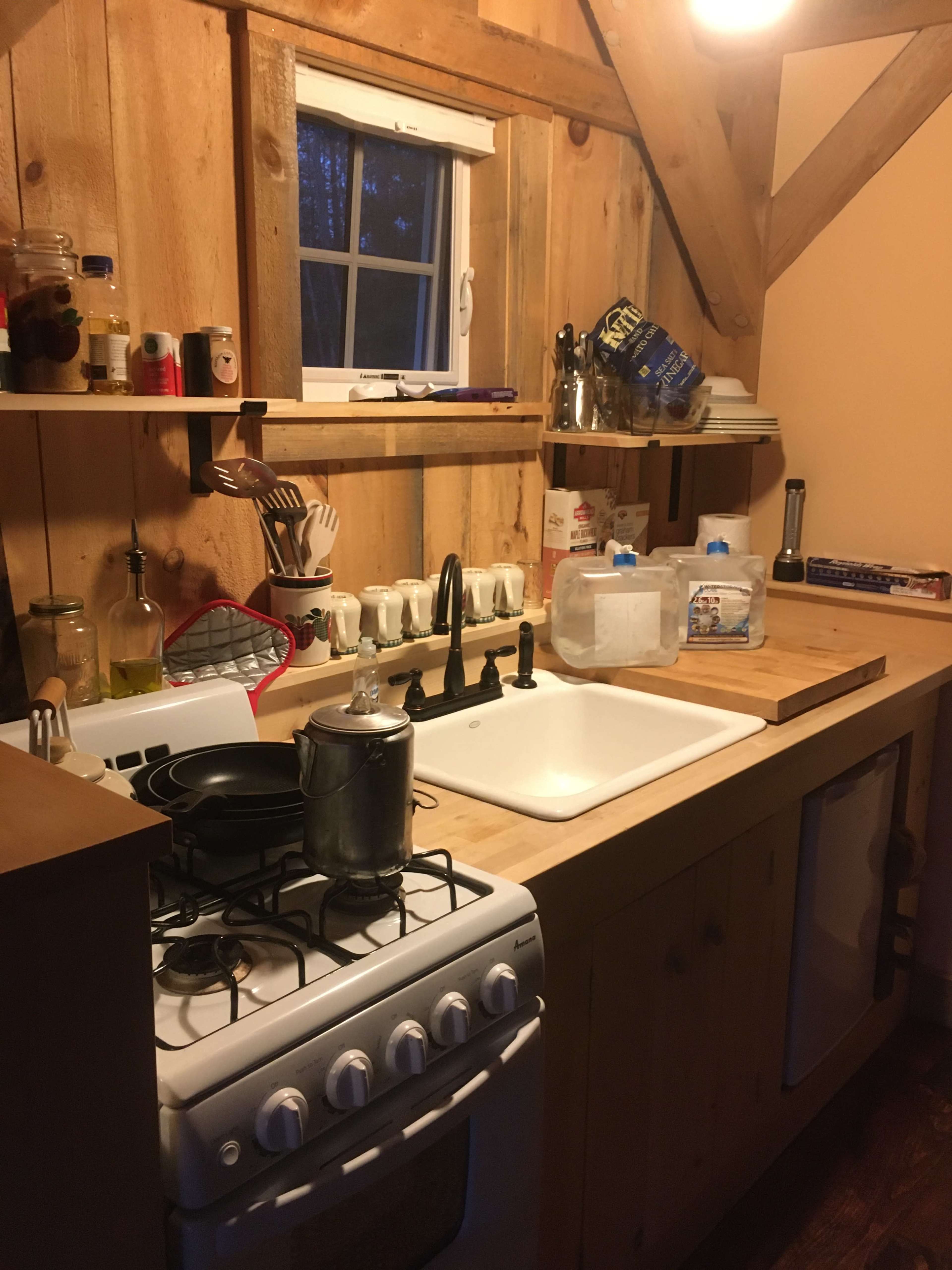 A wooden kitchen with a gas stove, a sink, and organized kitchenware on the countertop.