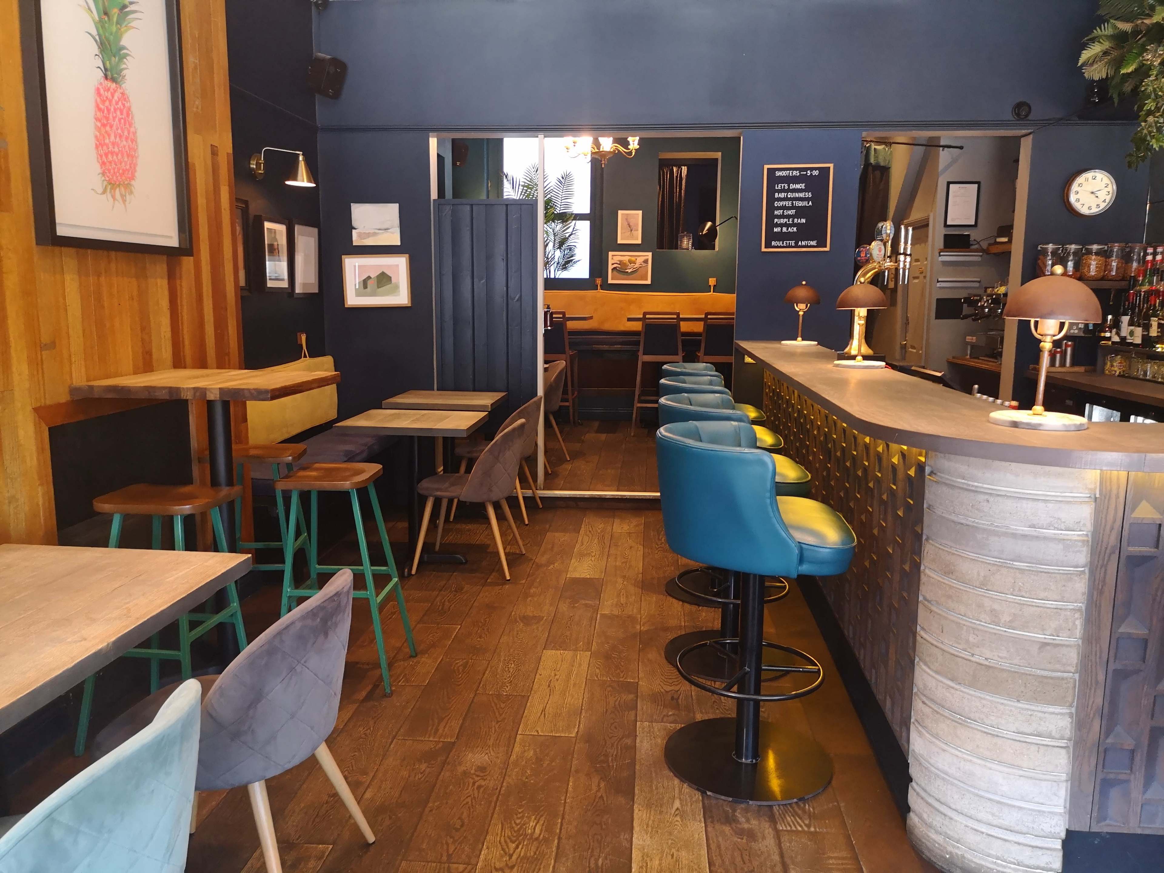 The image shows a modern café interior featuring a mix of wooden and upholstered seating, a curved bar, and artwork on the walls.