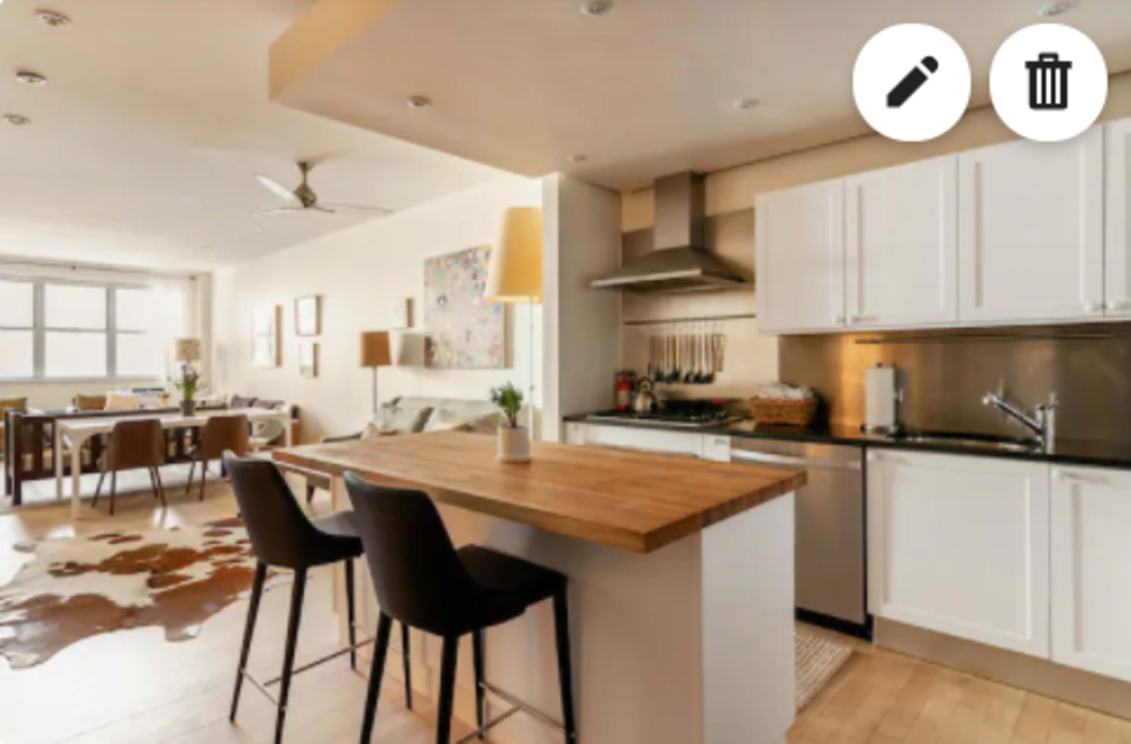 A modern kitchen with a wooden island and stools, open to a dining area featuring a table and chairs.