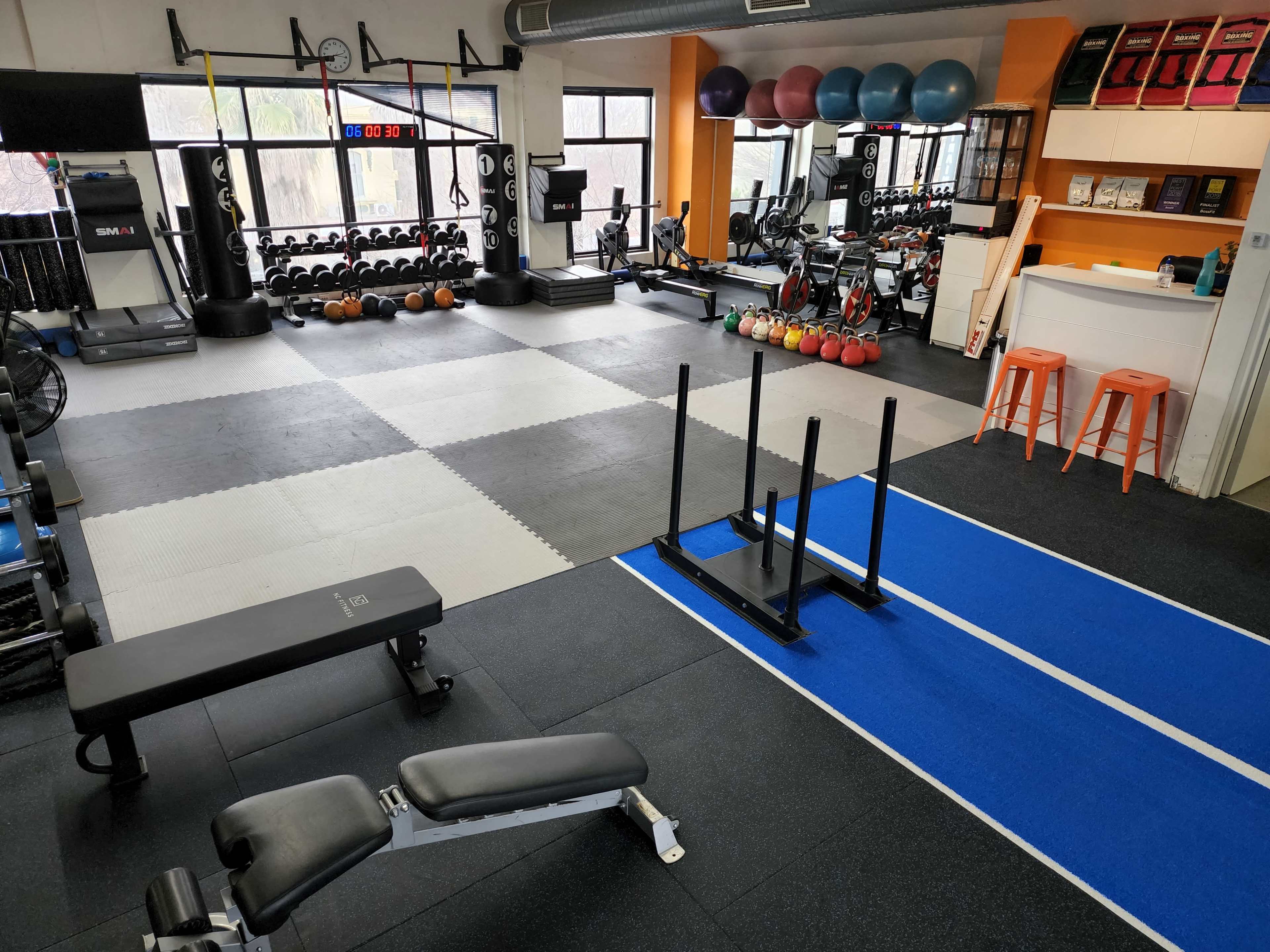 A gym interior with various exercise equipment, including weights, benches, and multifunctional machines, organized across rubber flooring sections.