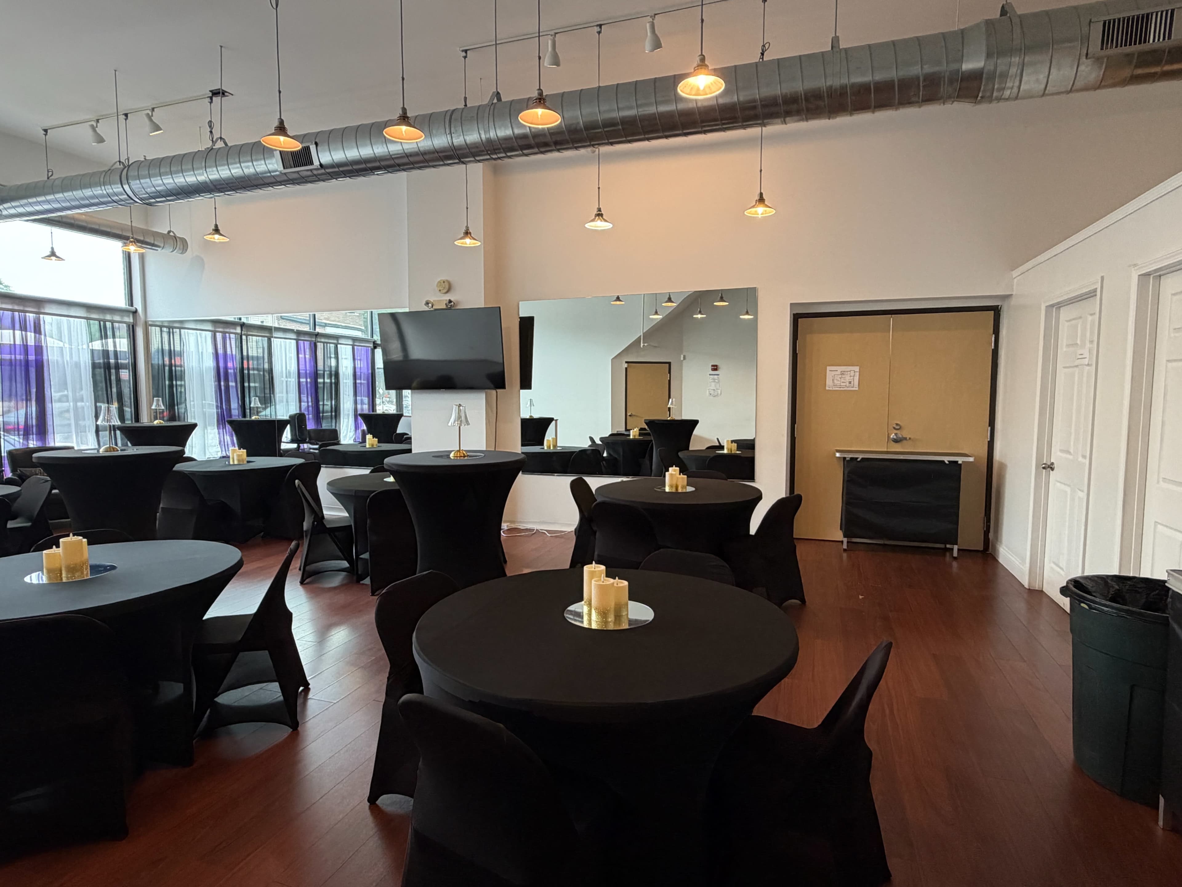 The image shows a banquet hall with round tables covered in black cloth, lit by overhead lights, and featuring candles on each table.
