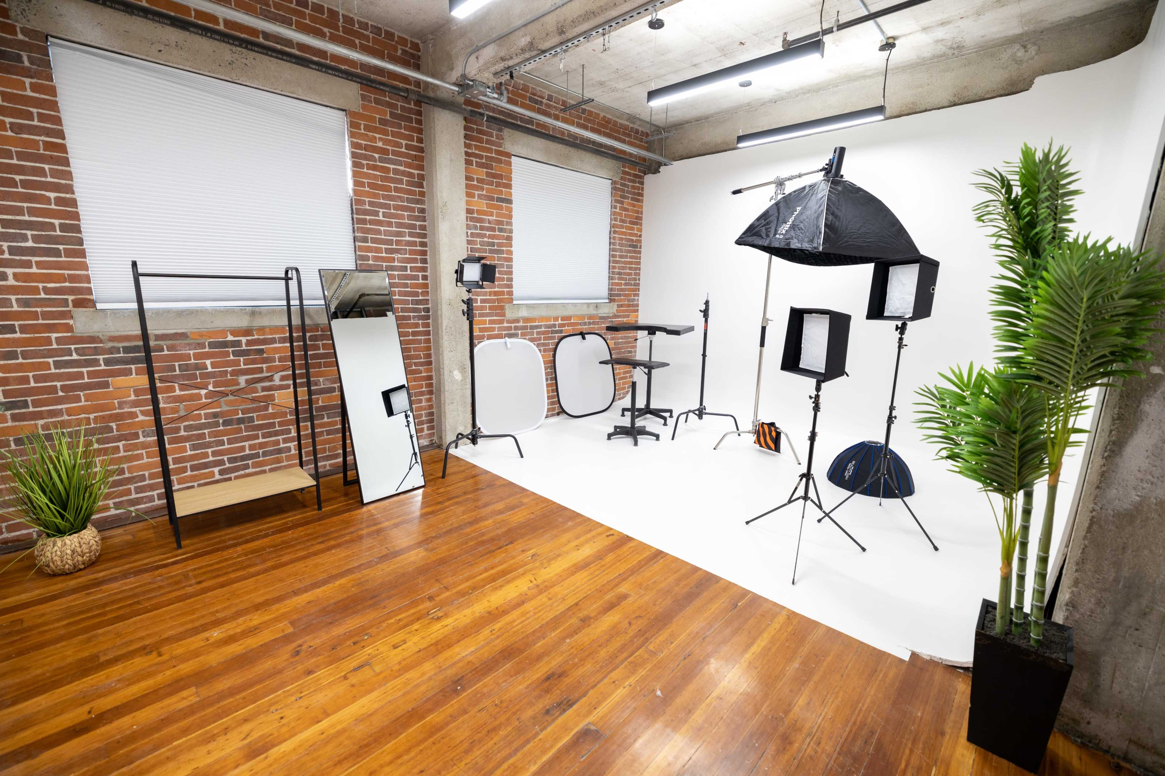 A photography studio with a white backdrop, lighting equipment, and props arranged around a wooden floor.