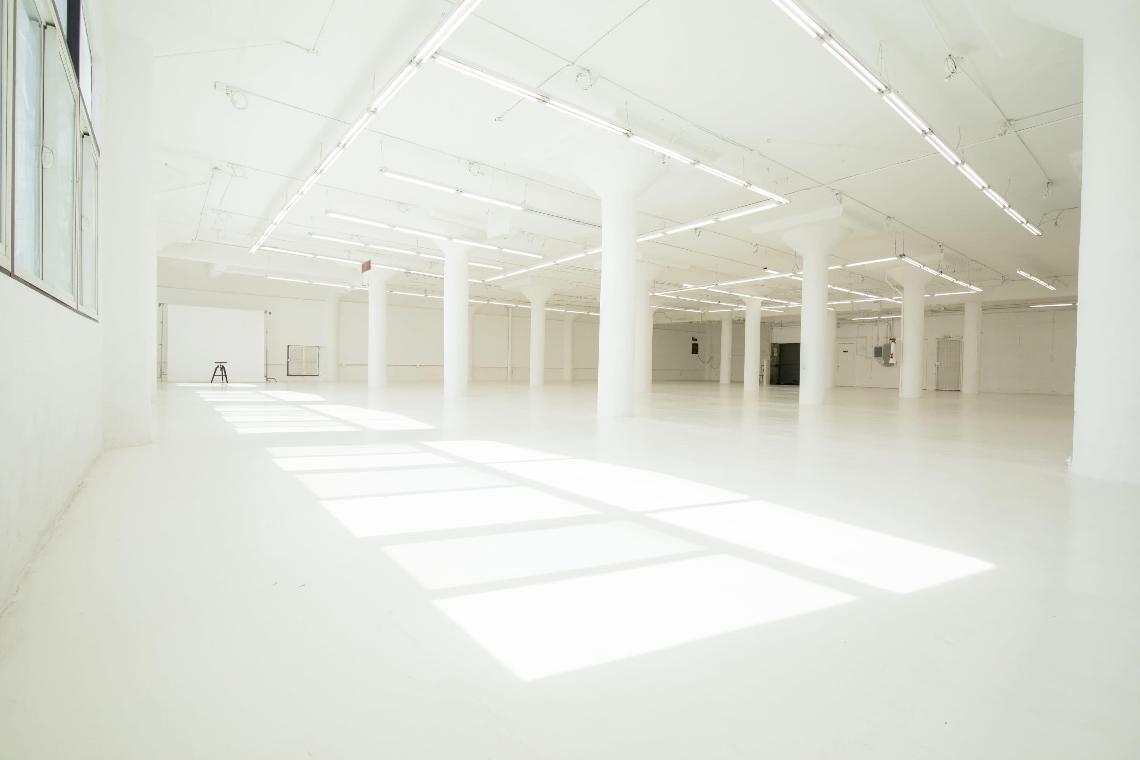 The image shows a large, empty, well-lit room with white walls and numerous columns.