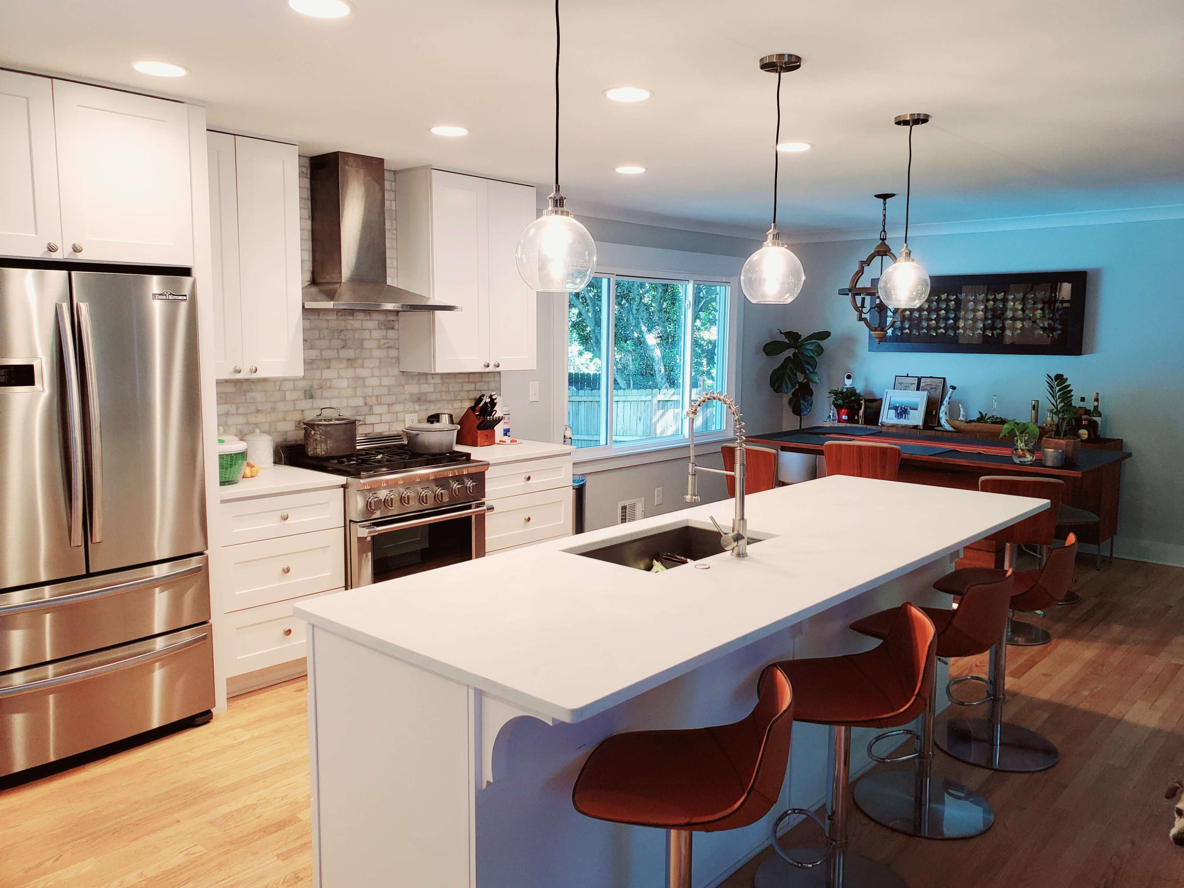 The kitchen features a large island with modern bar stools, stainless steel appliances, and a window overlooking a backyard.