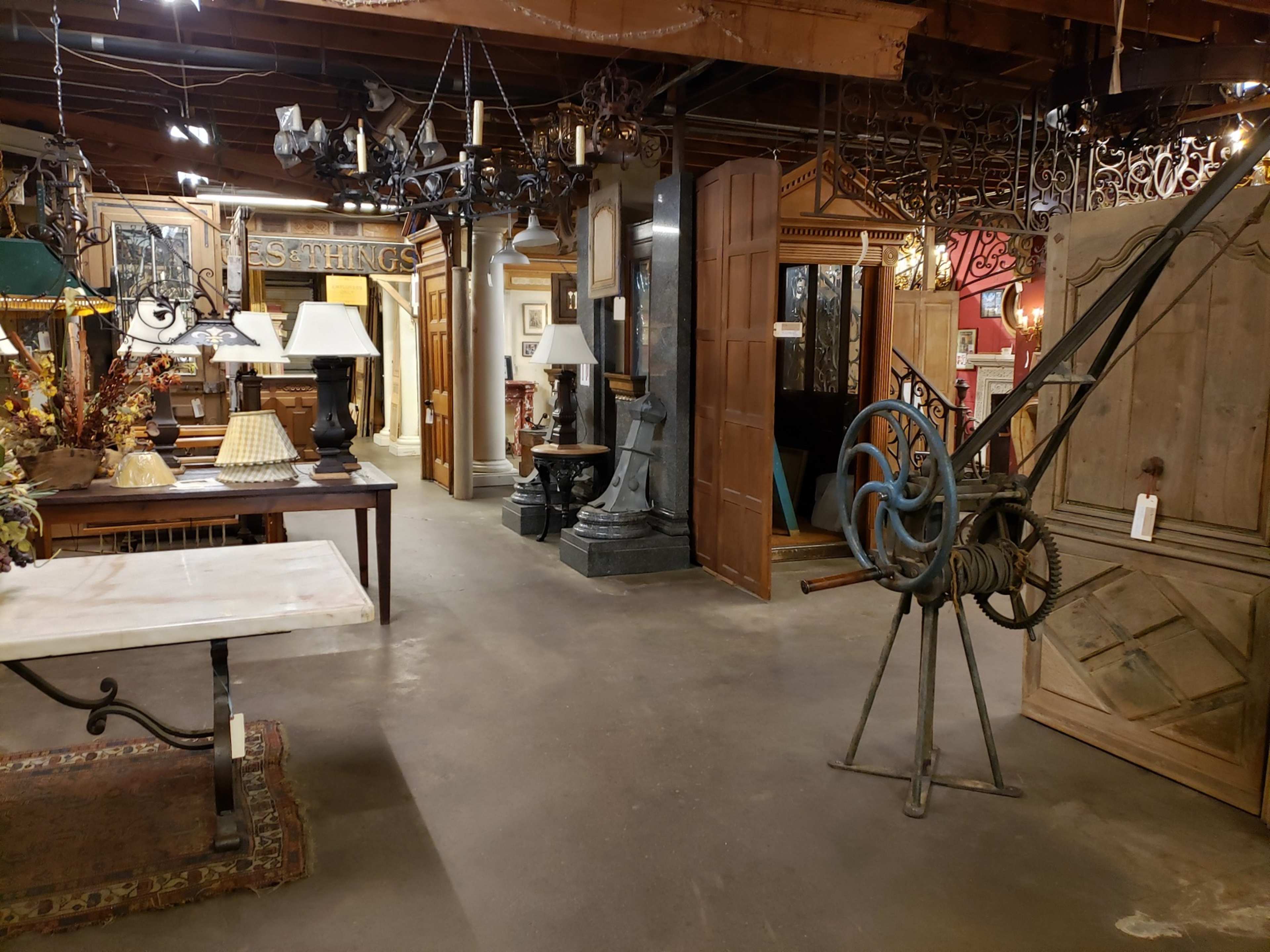 The image shows an antique store interior filled with various vintage items, including furniture, lamps, and decorative pieces, under a wooden beam ceiling.