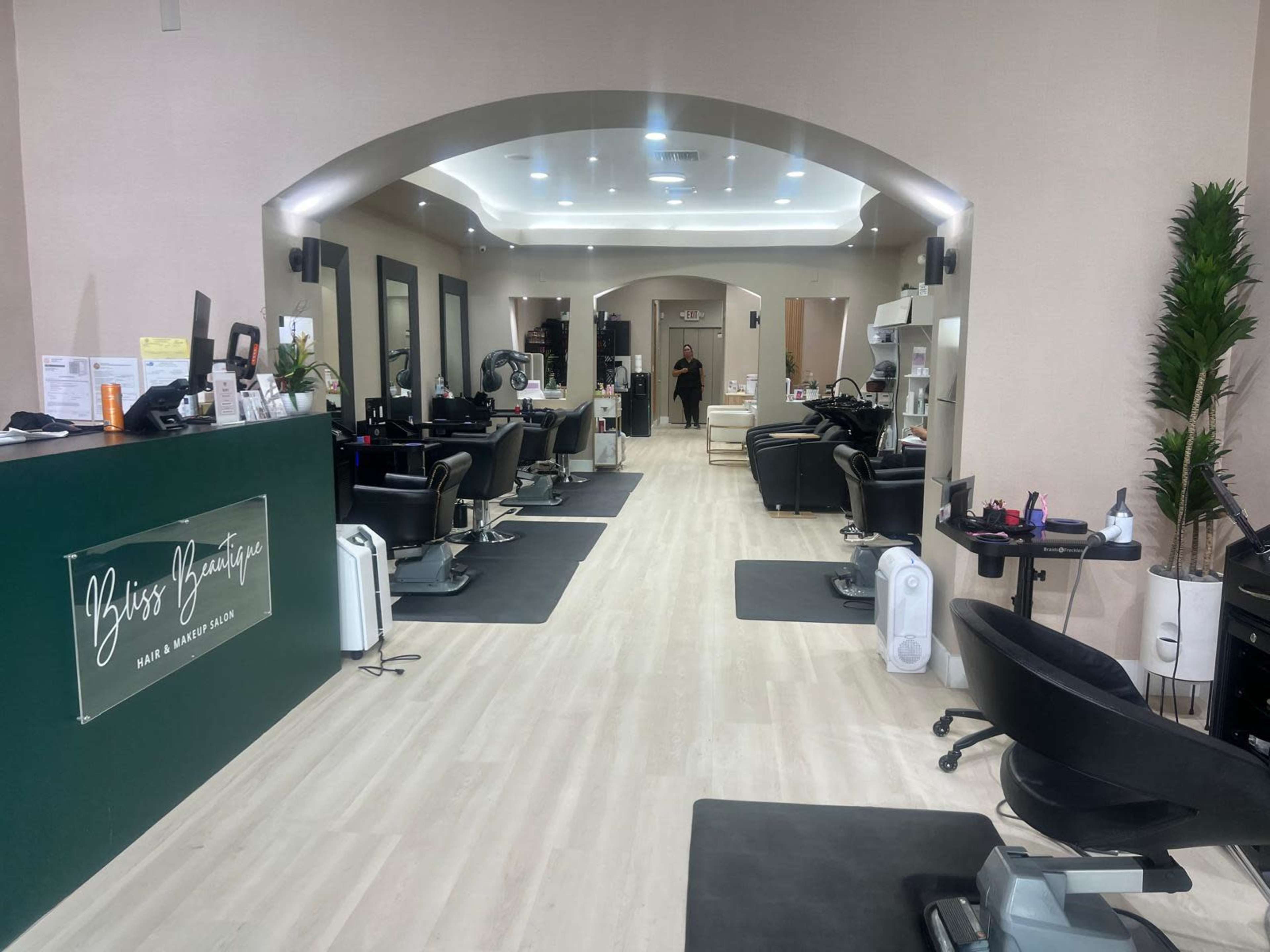 The image shows the interior of a hair salon with multiple styling stations, a reception desk, and a bright, open layout.