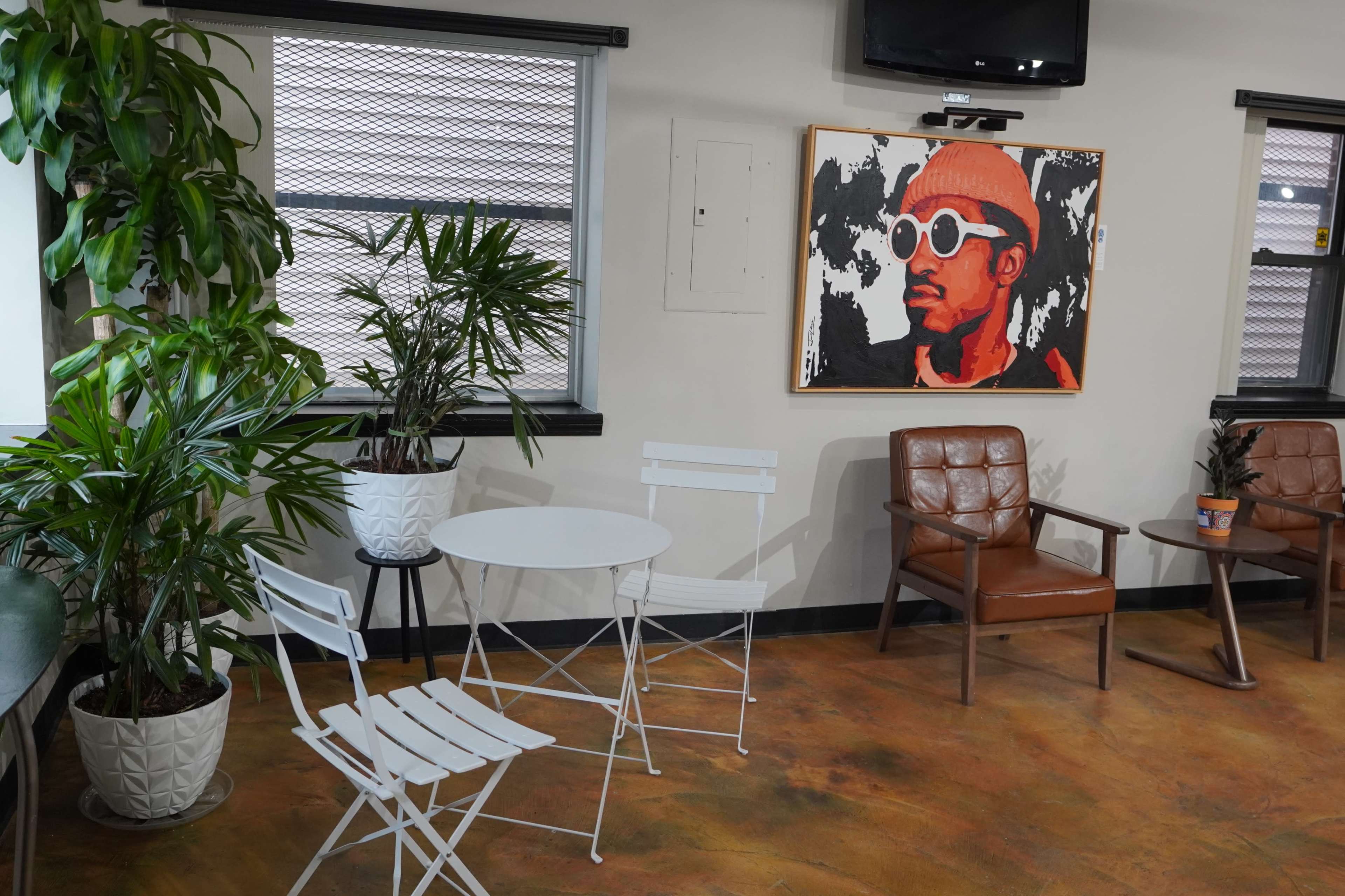A small indoor seating area featuring a white table and chairs, two potted plants, and a large portrait on the wall.