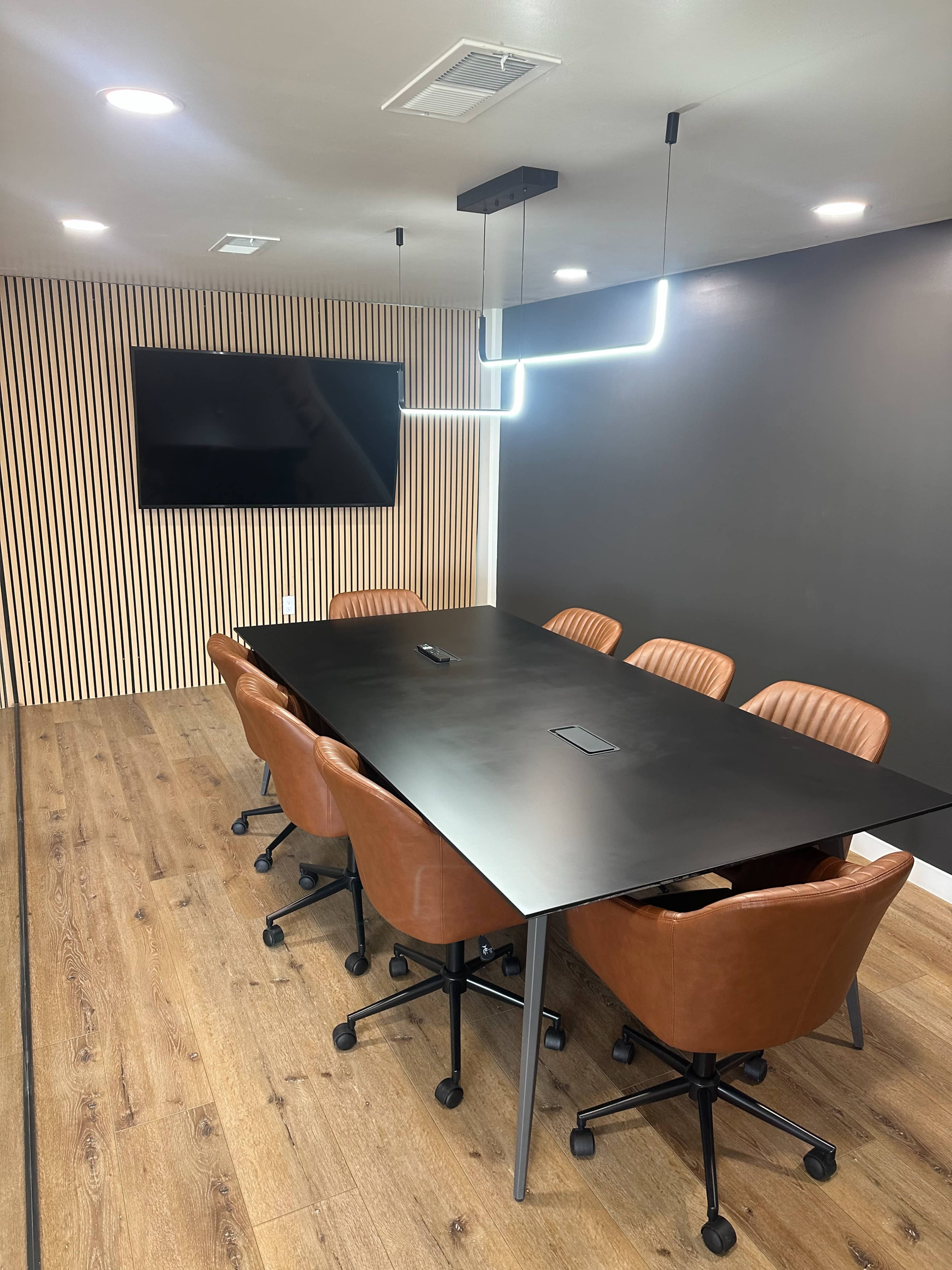 A conference room features a long black table surrounded by brown leather chairs and a large wall-mounted TV.