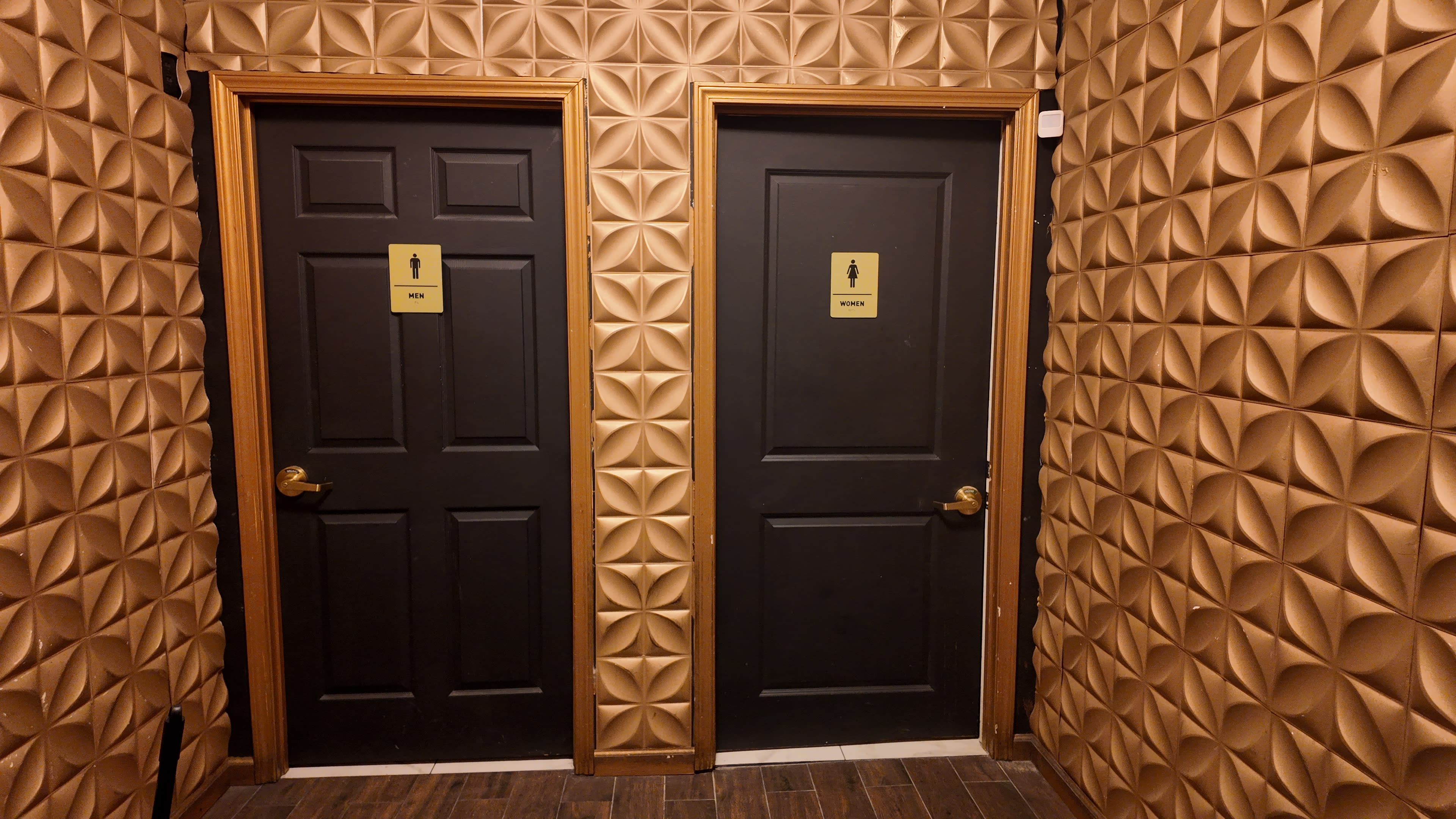 The image shows two black doors labeled "Men" and "Women" in a hallway with textured gold walls.