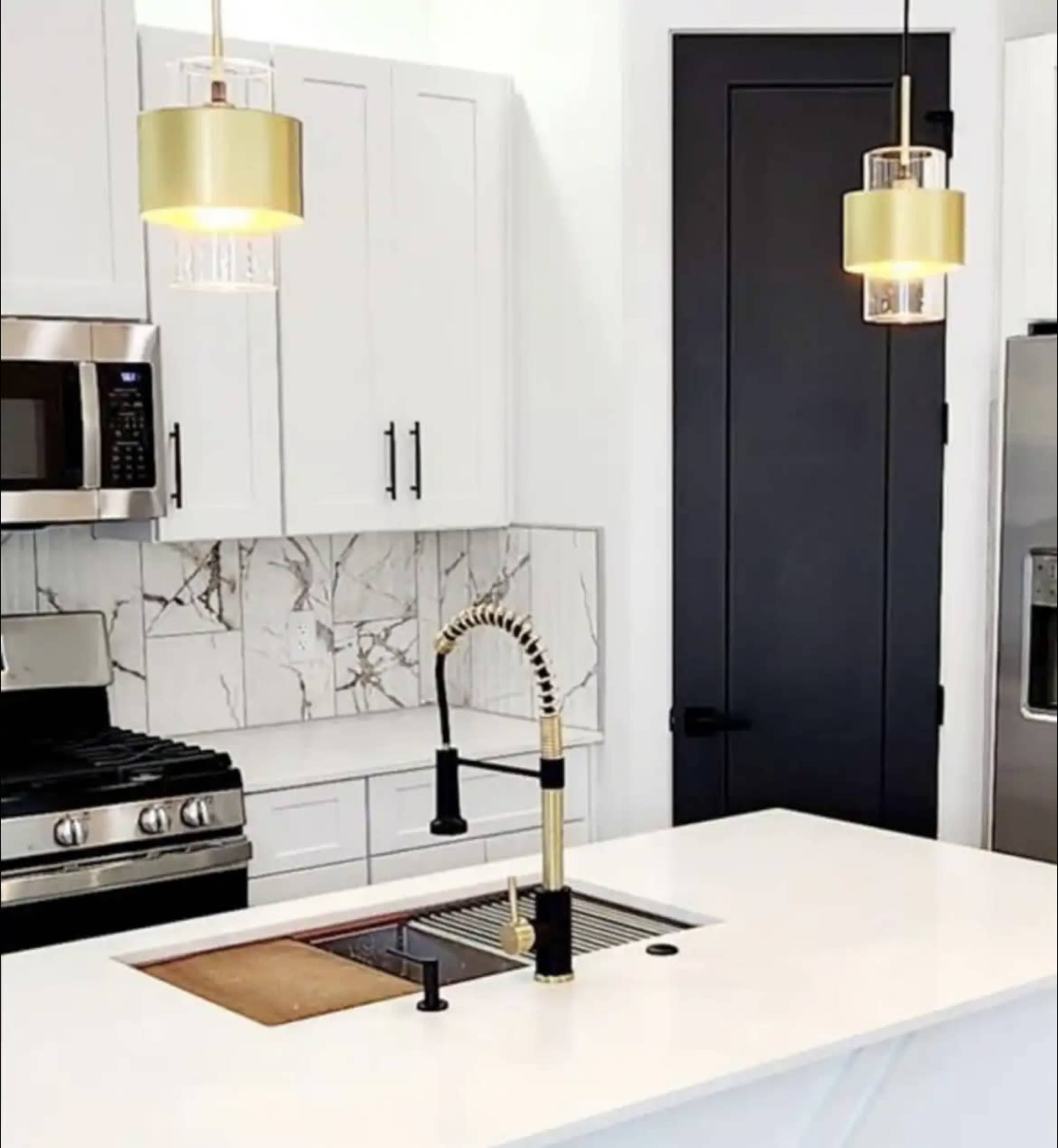 A modern kitchen featuring a stainless steel stove, white cabinetry, a gold-accented faucet, and pendant lights above a white countertop.