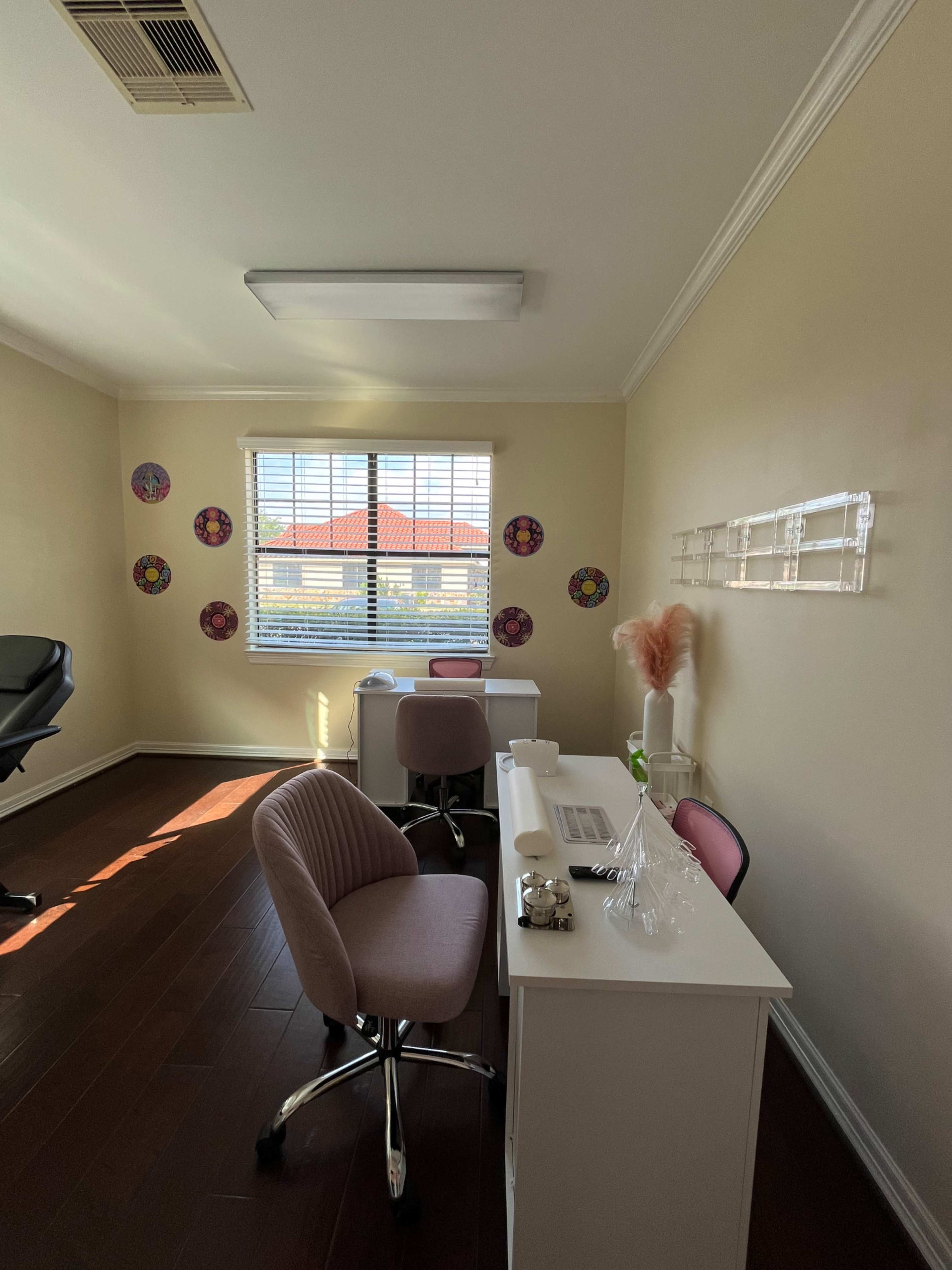 The image shows a brightly lit office space with two white desks, pink accent chairs, and colorful decorative plates on the walls.