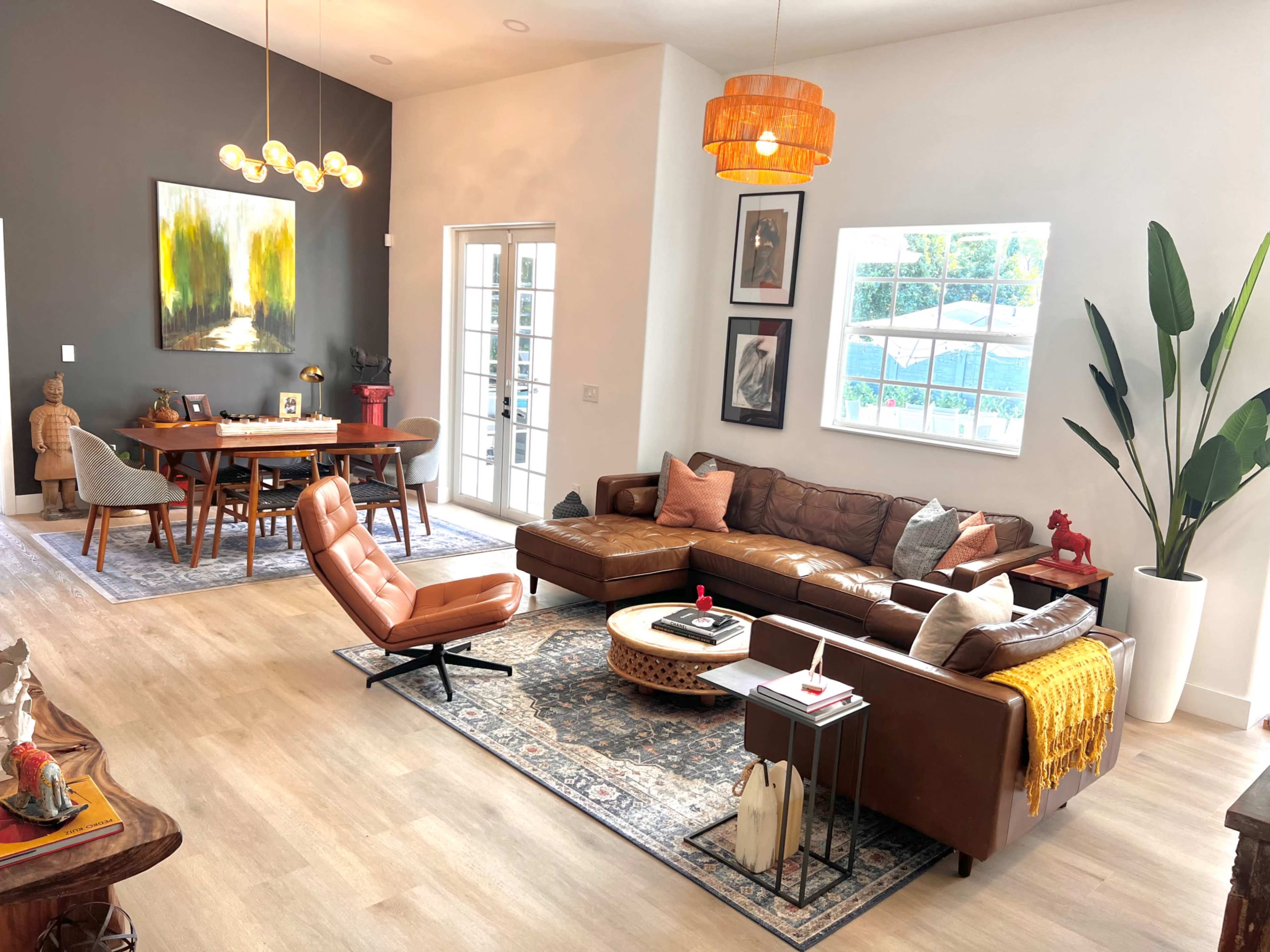 A modern living room and dining area featuring a large brown leather sectional sofa, a wooden dining table, and decorative plants.