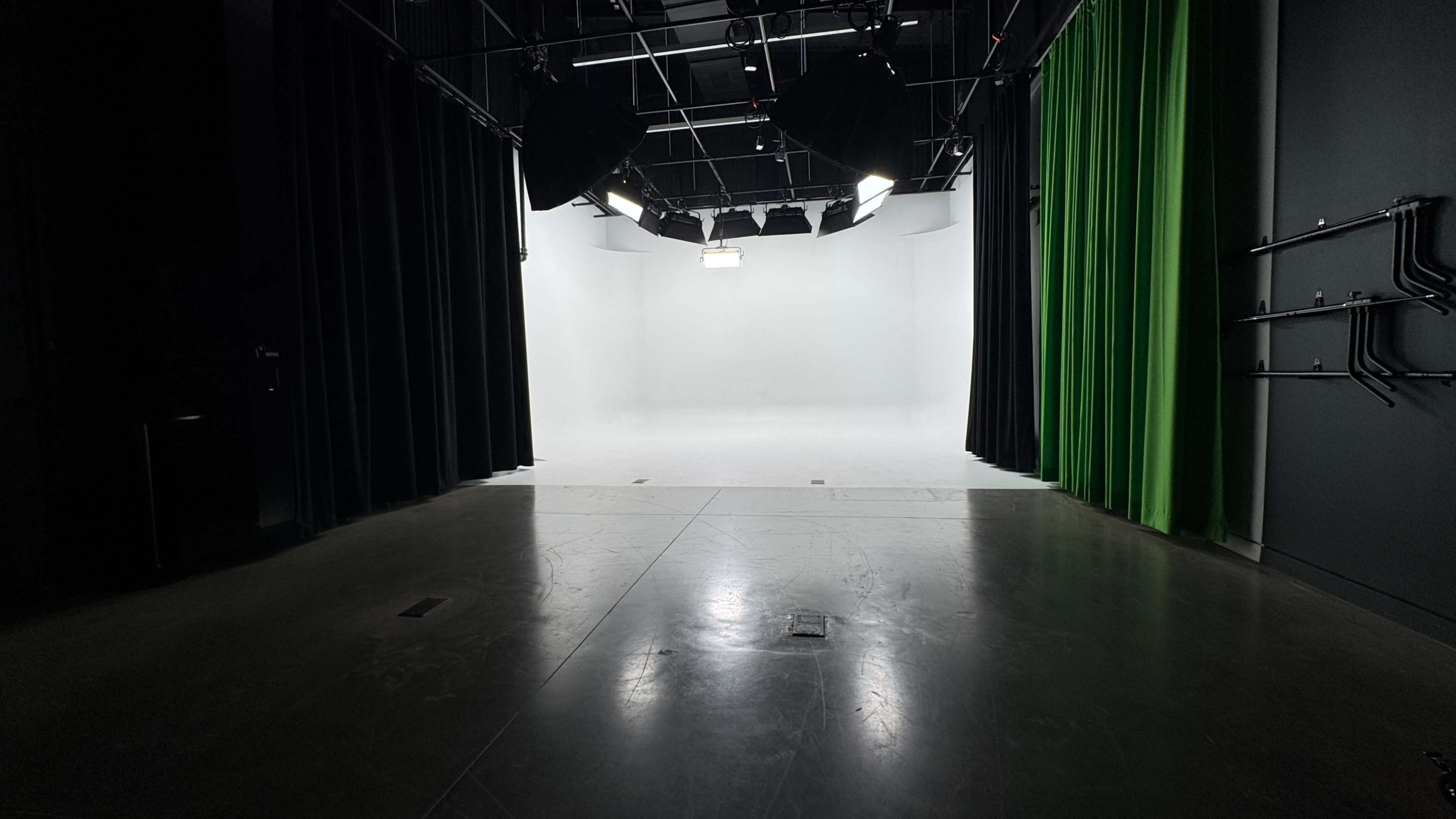 The image shows a spacious studio with a bright white backdrop, complemented by black curtains on one side and a green curtain on the other.