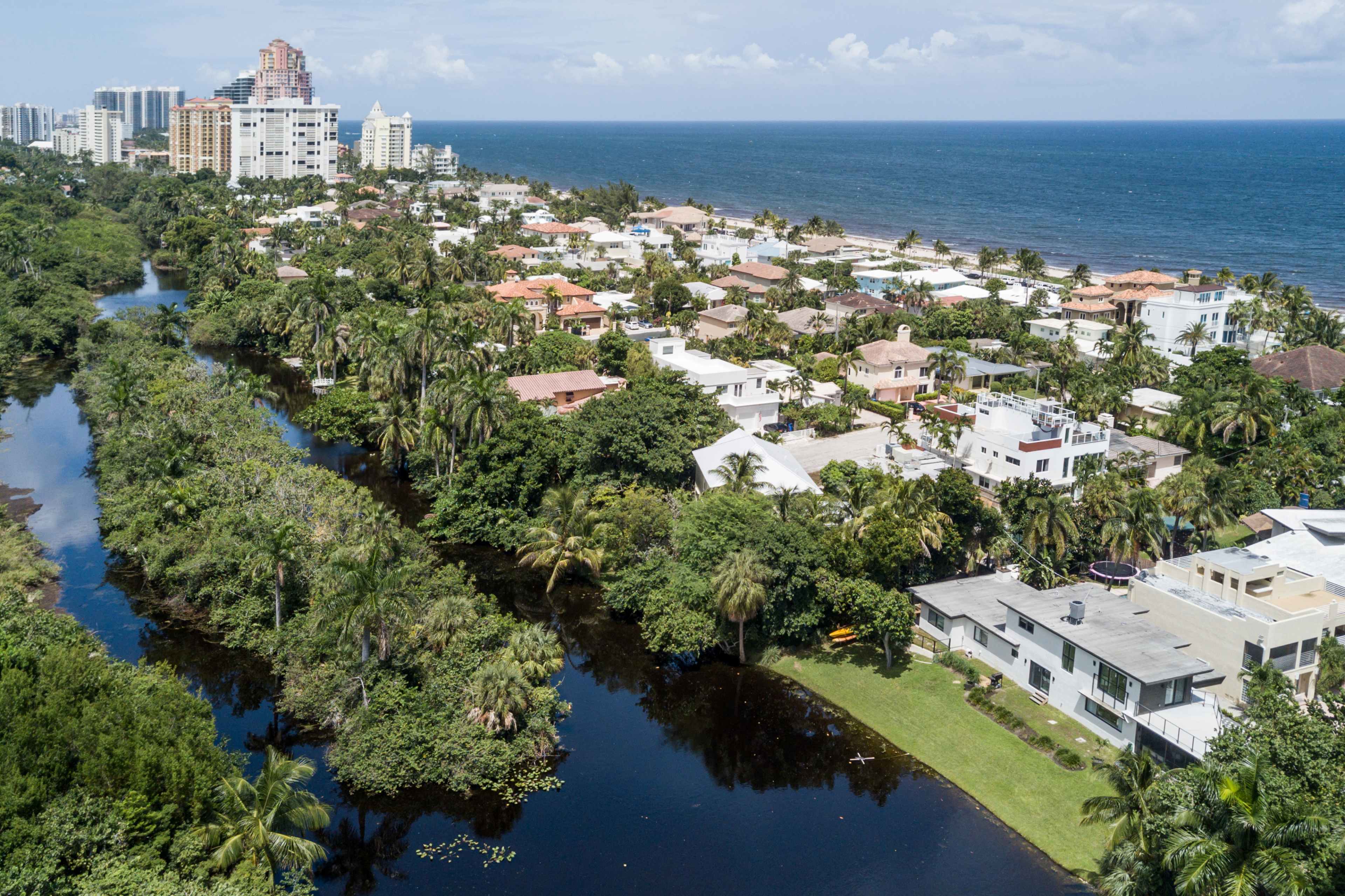 The image shows a coastal residential area with houses lining a waterway and the ocean visible in the background.