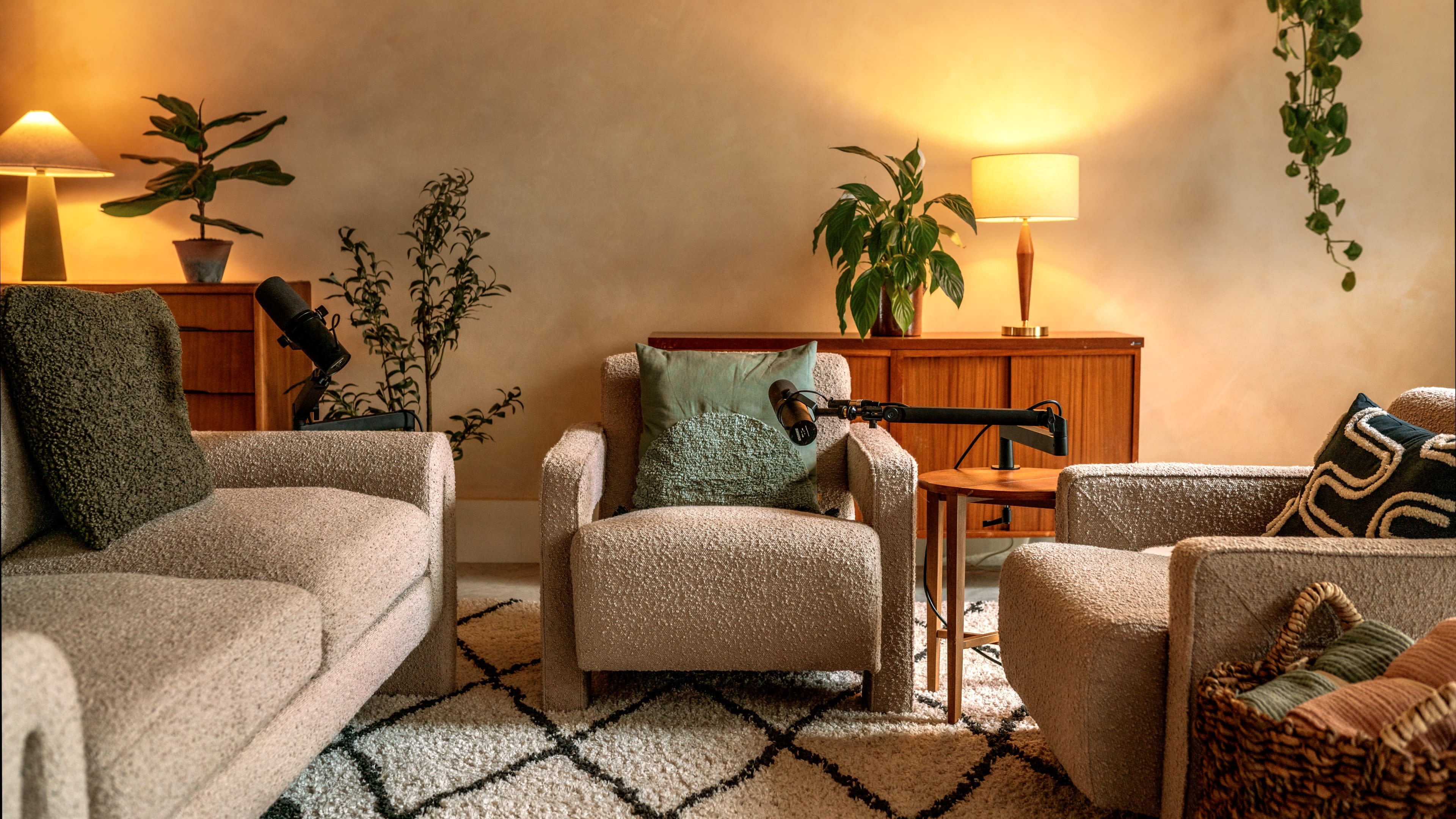 The image shows a cozy living room with two textured armchairs, a small wooden side table, and greenery, illuminated by soft lamps.