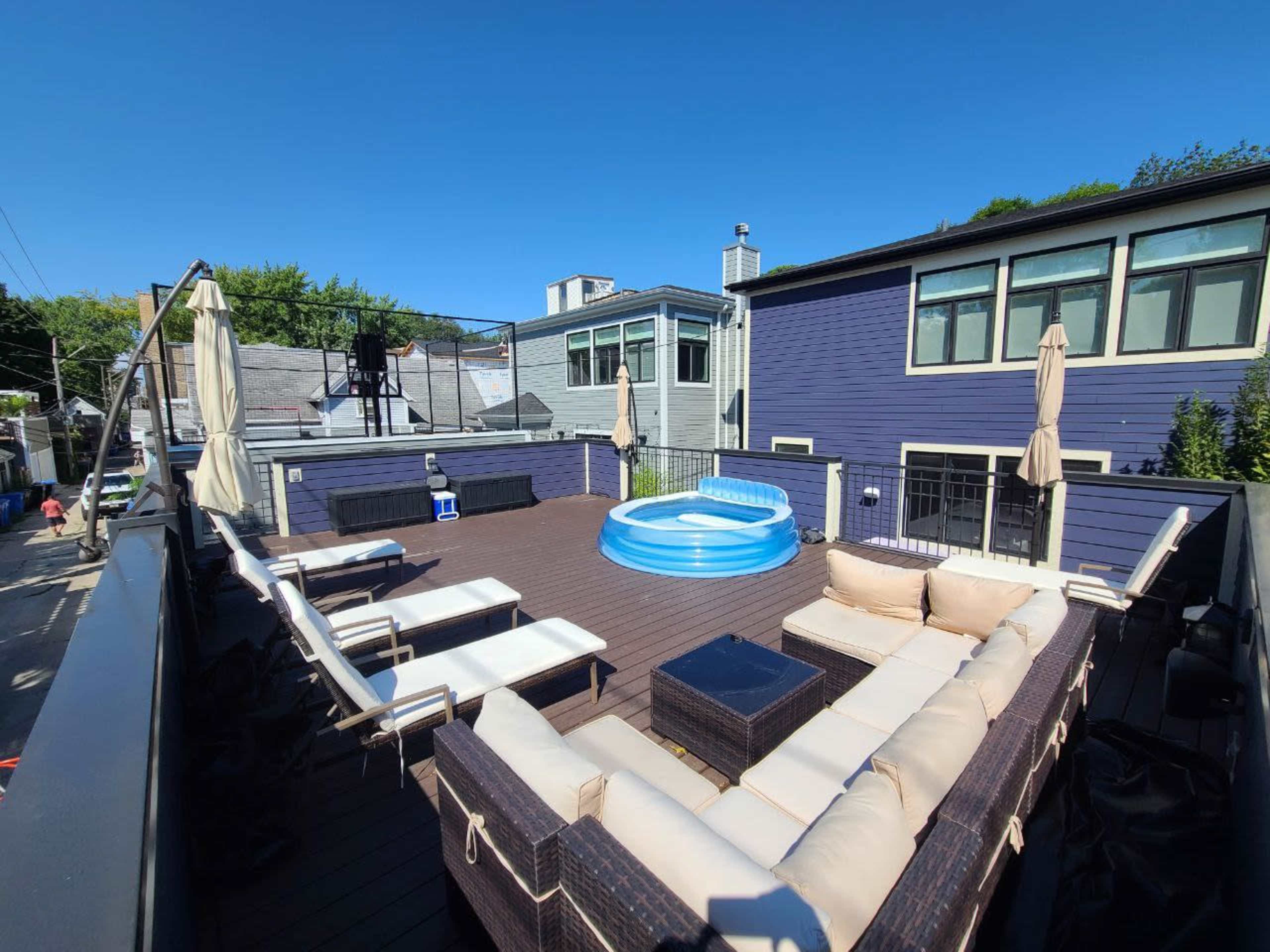 A rooftop deck featuring a circular inflatable pool, several lounge chairs, and a seating area with a sectional sofa under clear blue skies.