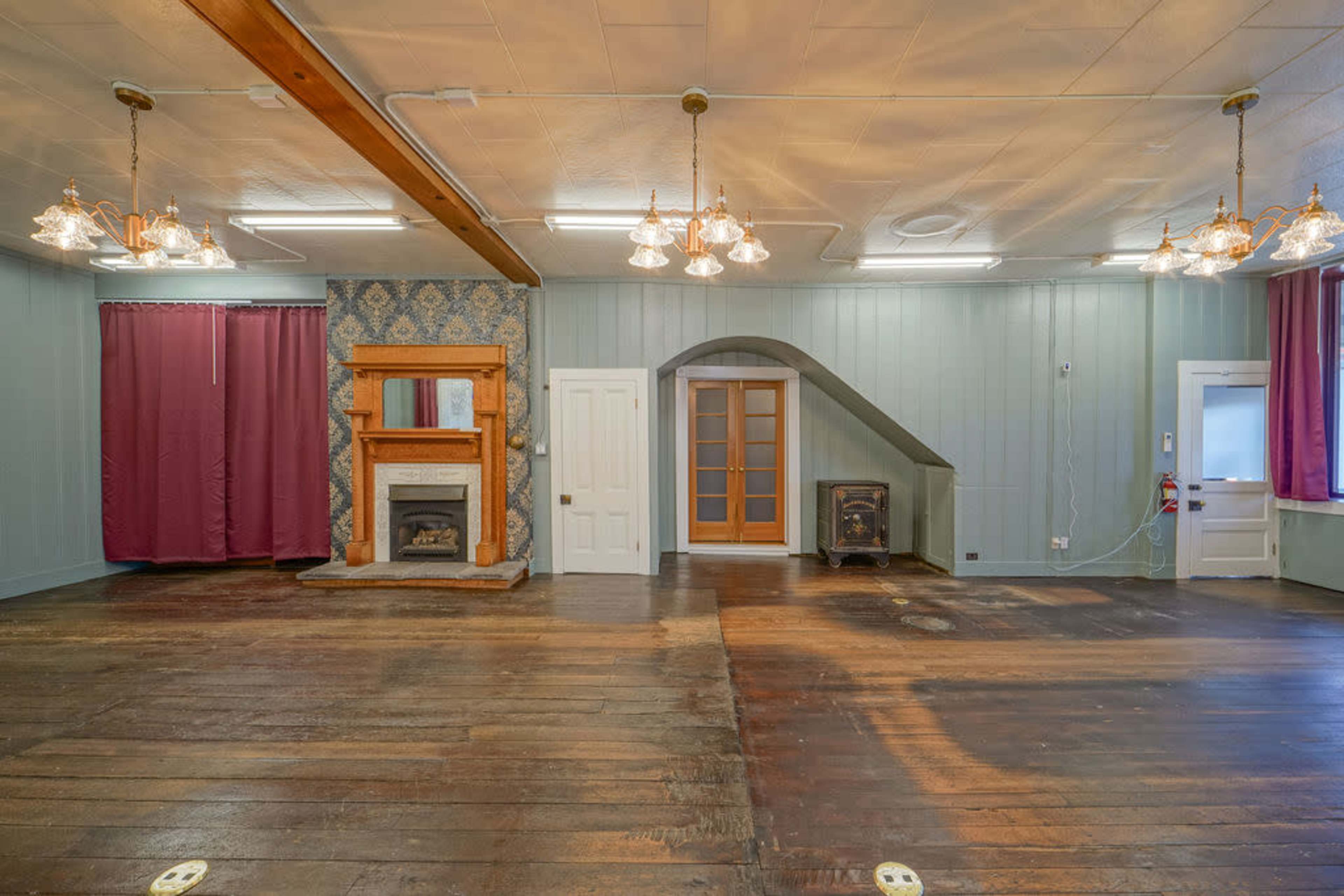 The image shows a spacious interior room with wooden floors, a fireplace, and decorative wall features, highlighted by purple curtains and multiple light fixtures.