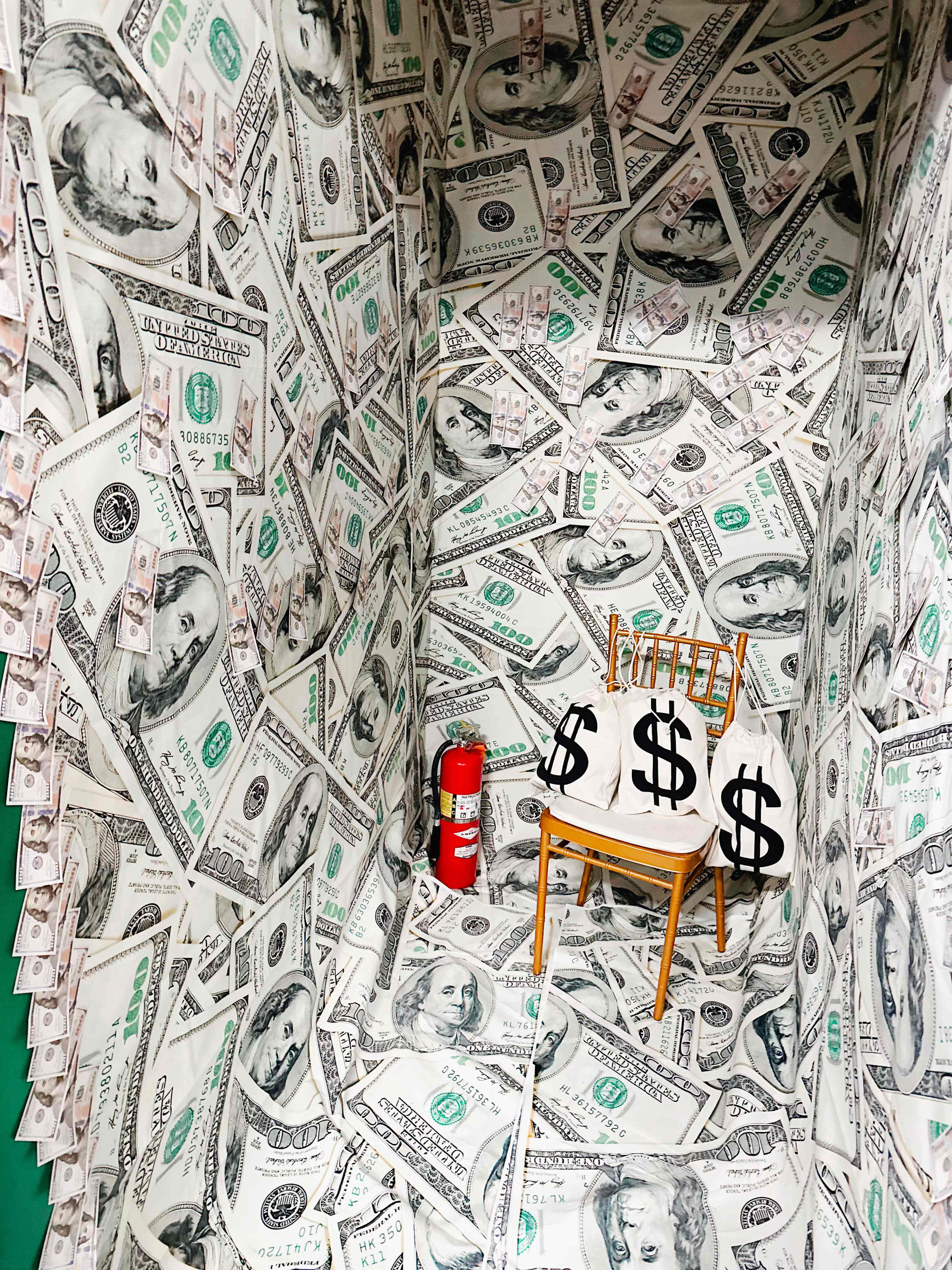 A small room with walls and floor covered in printed dollar bills, featuring a gold chair and a fire extinguisher.