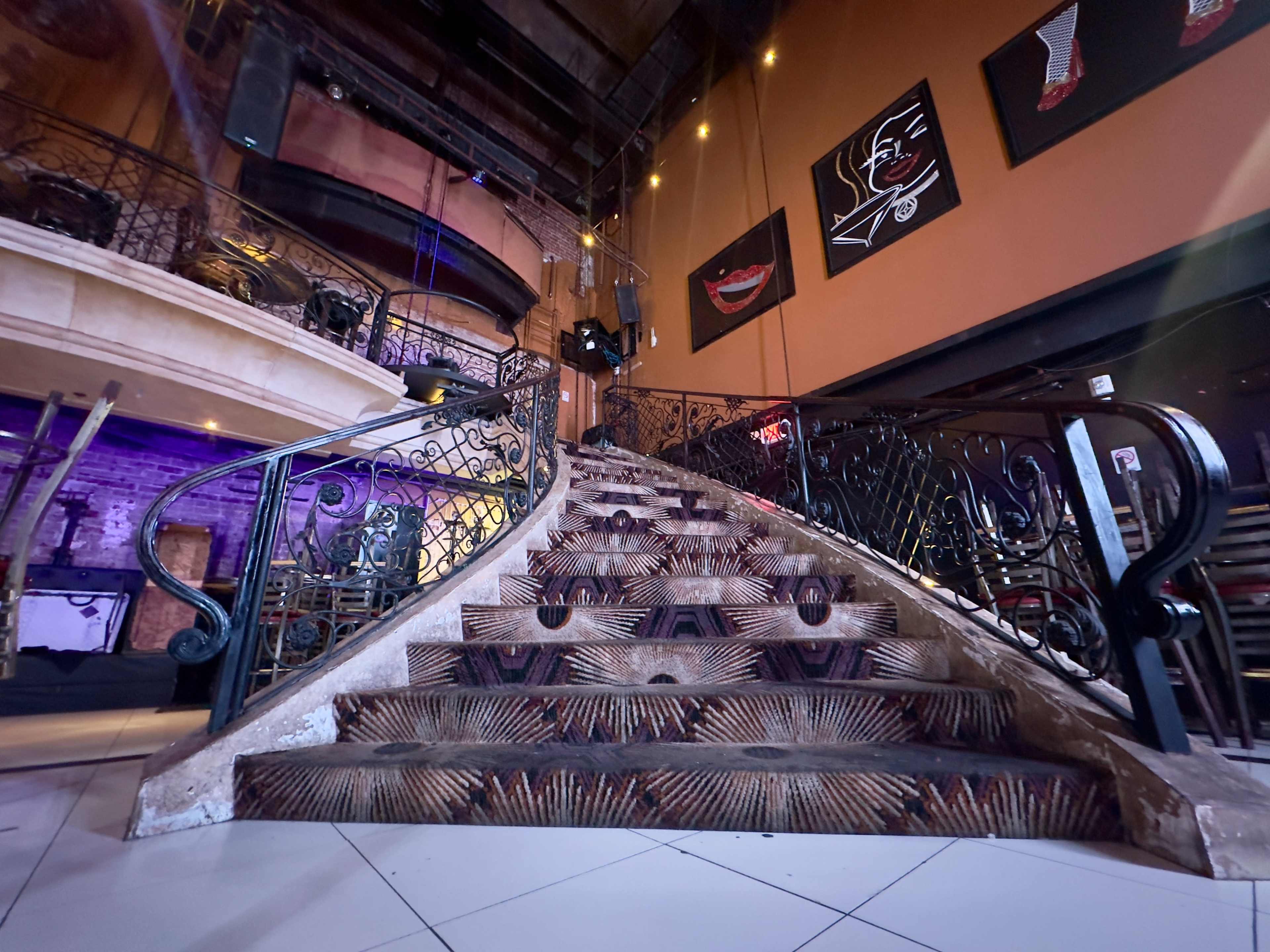 The image shows a decorated staircase leading up from a brightly lit lounge area with artistic murals on the walls.