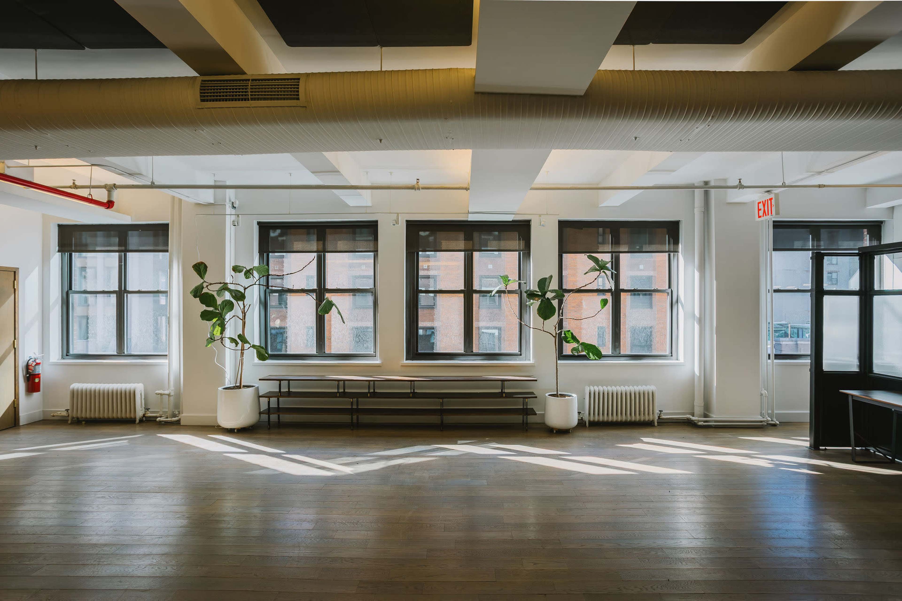 The image shows a modern, spacious office interior with large windows, wooden flooring, and minimalistic furniture.