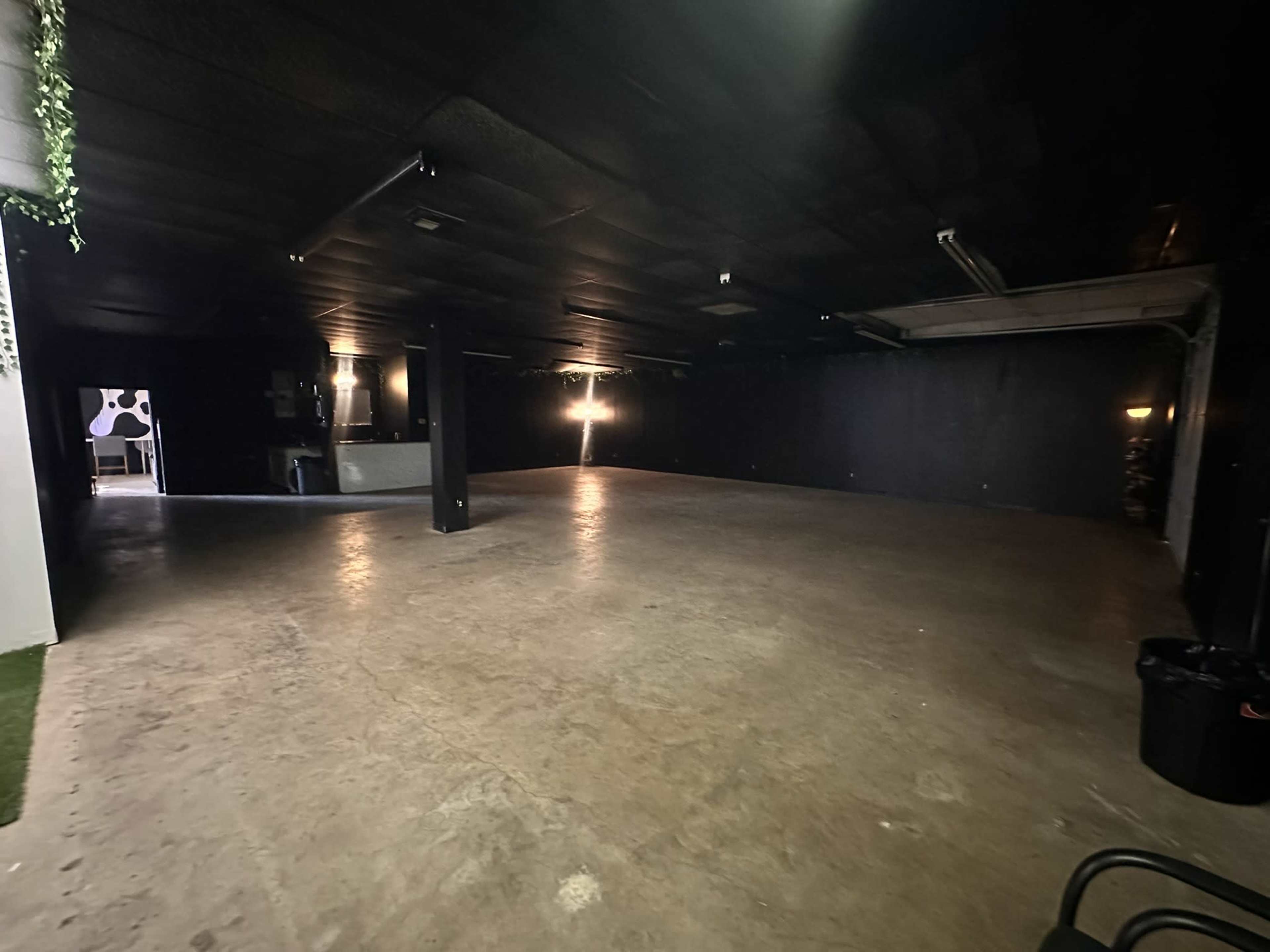 The image shows a spacious, dimly lit room with black walls and a concrete floor.