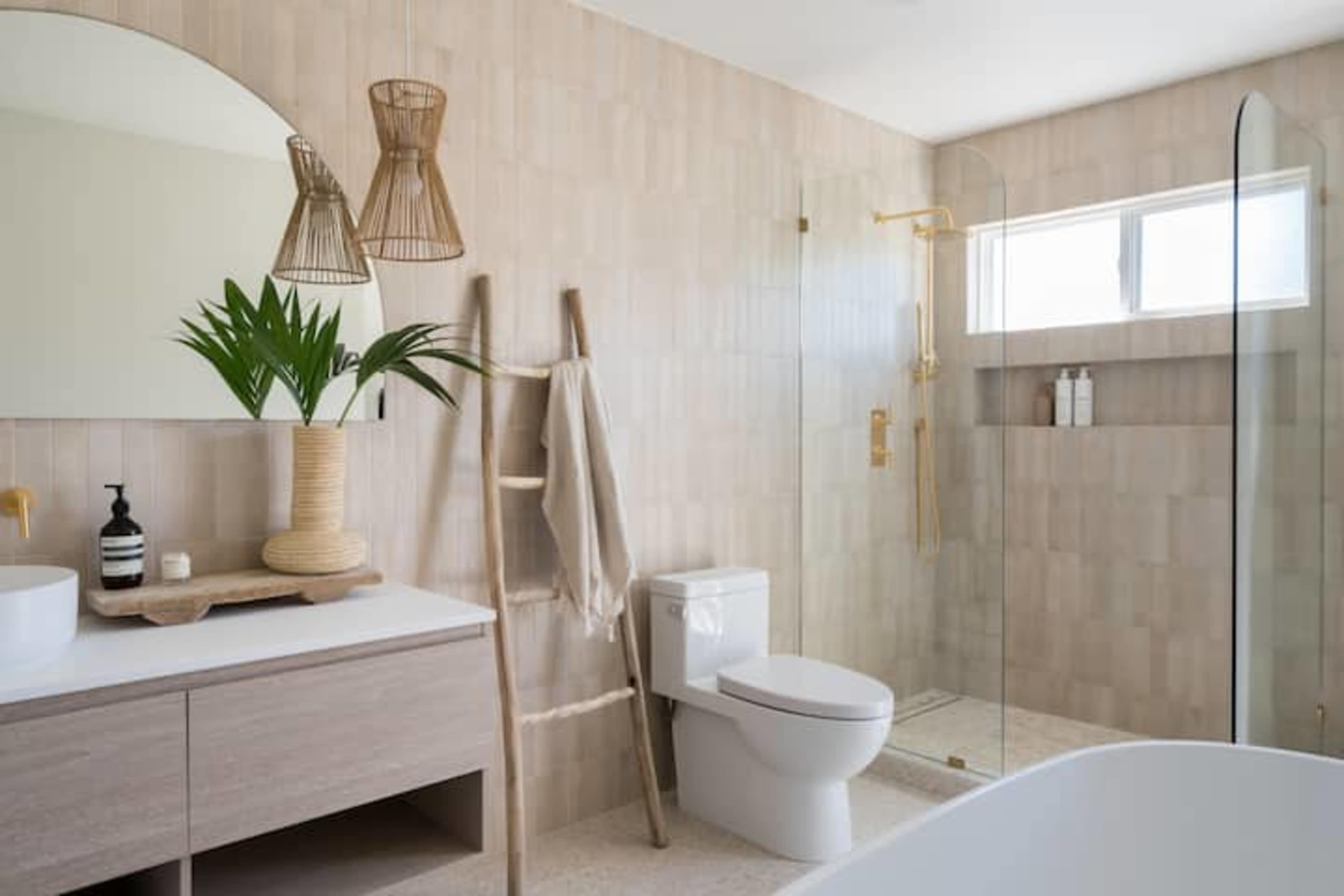 A modern bathroom features a glass shower, a freestanding tub, a wooden vanity, and natural decor elements such as a plant and a bamboo ladder.