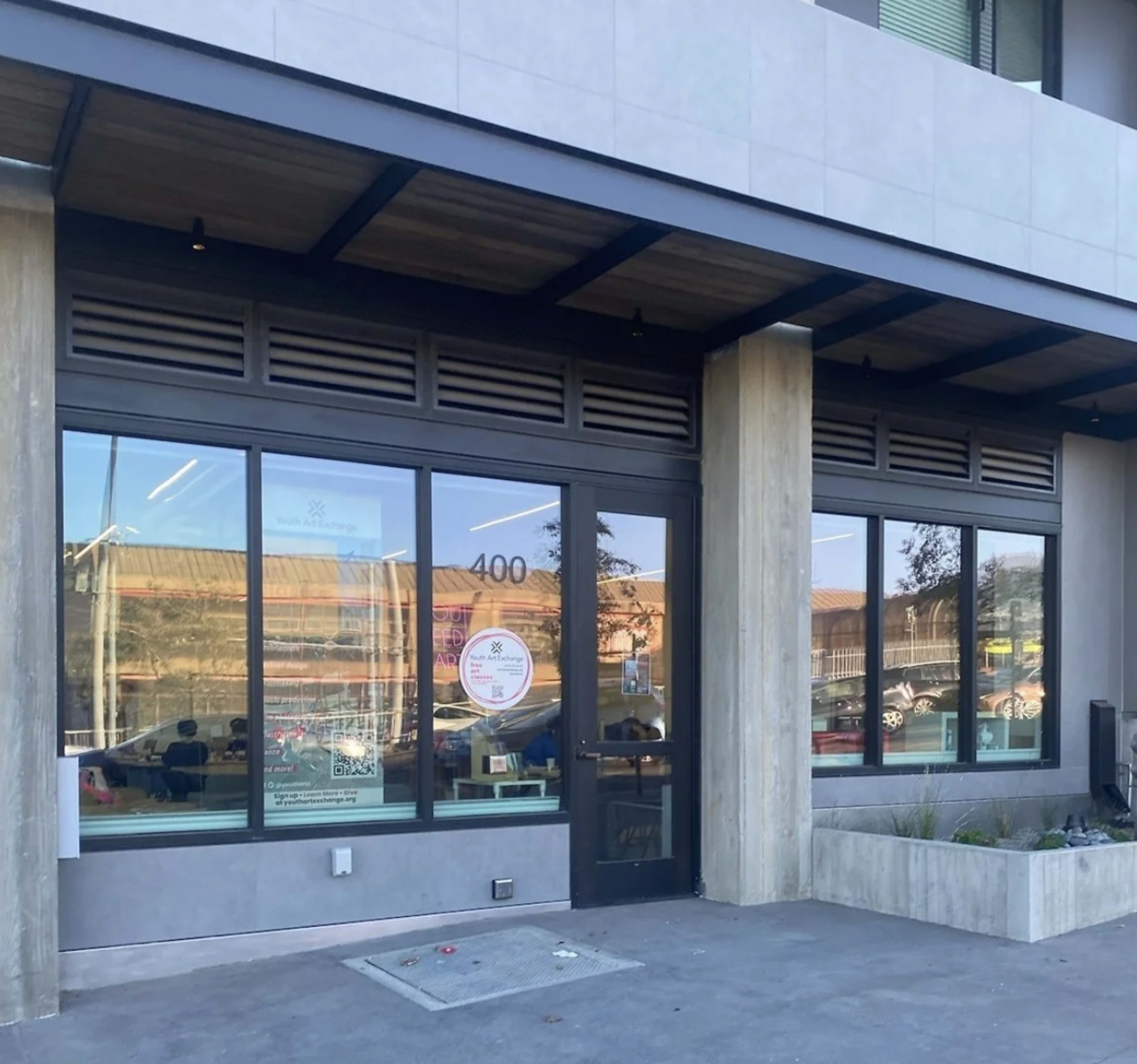 The image shows the exterior of a modern building with large windows and a gray facade, featuring a main entrance door labeled "400."