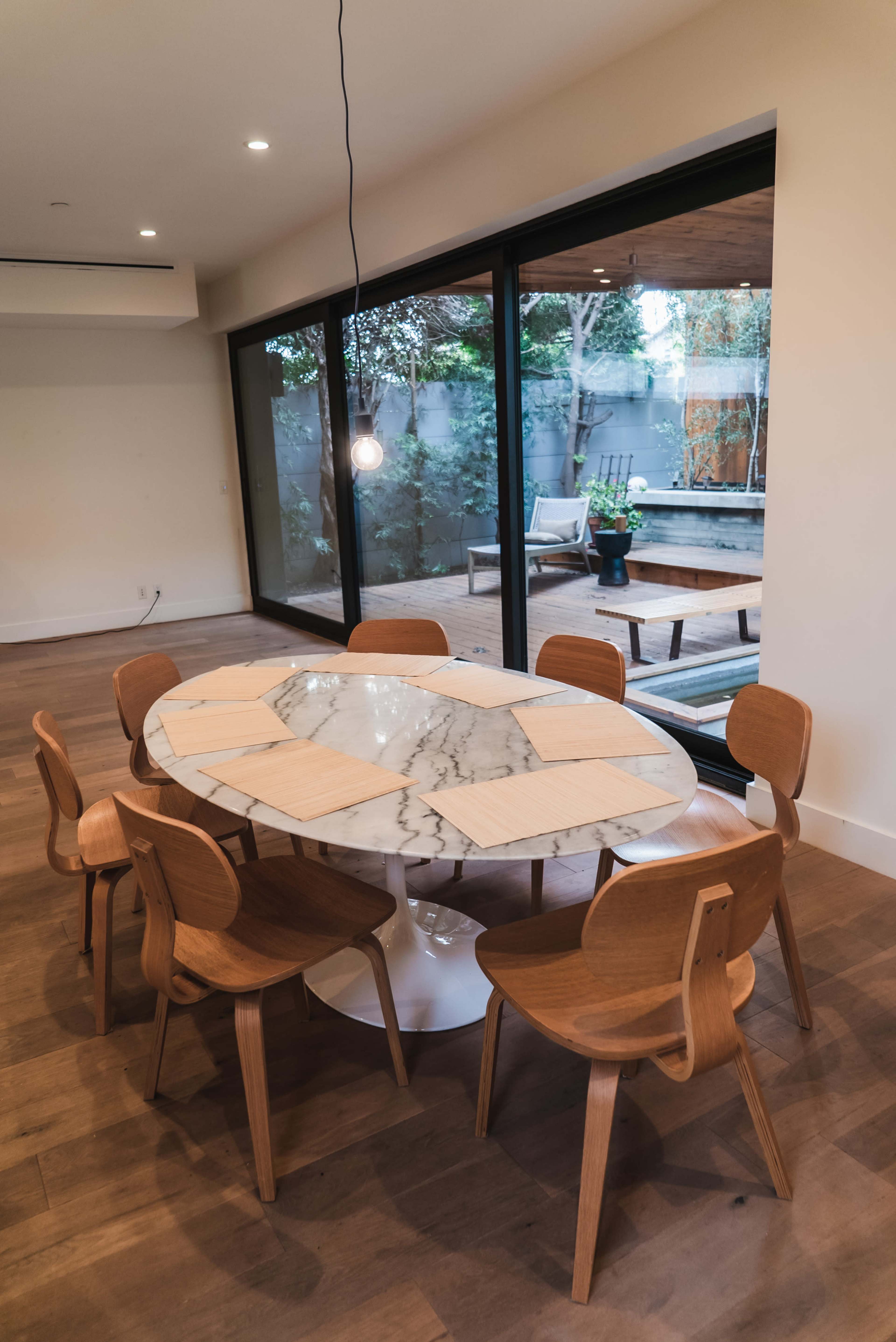 A round marble dining table is surrounded by wooden chairs in a room with large glass doors leading to a patio area.
