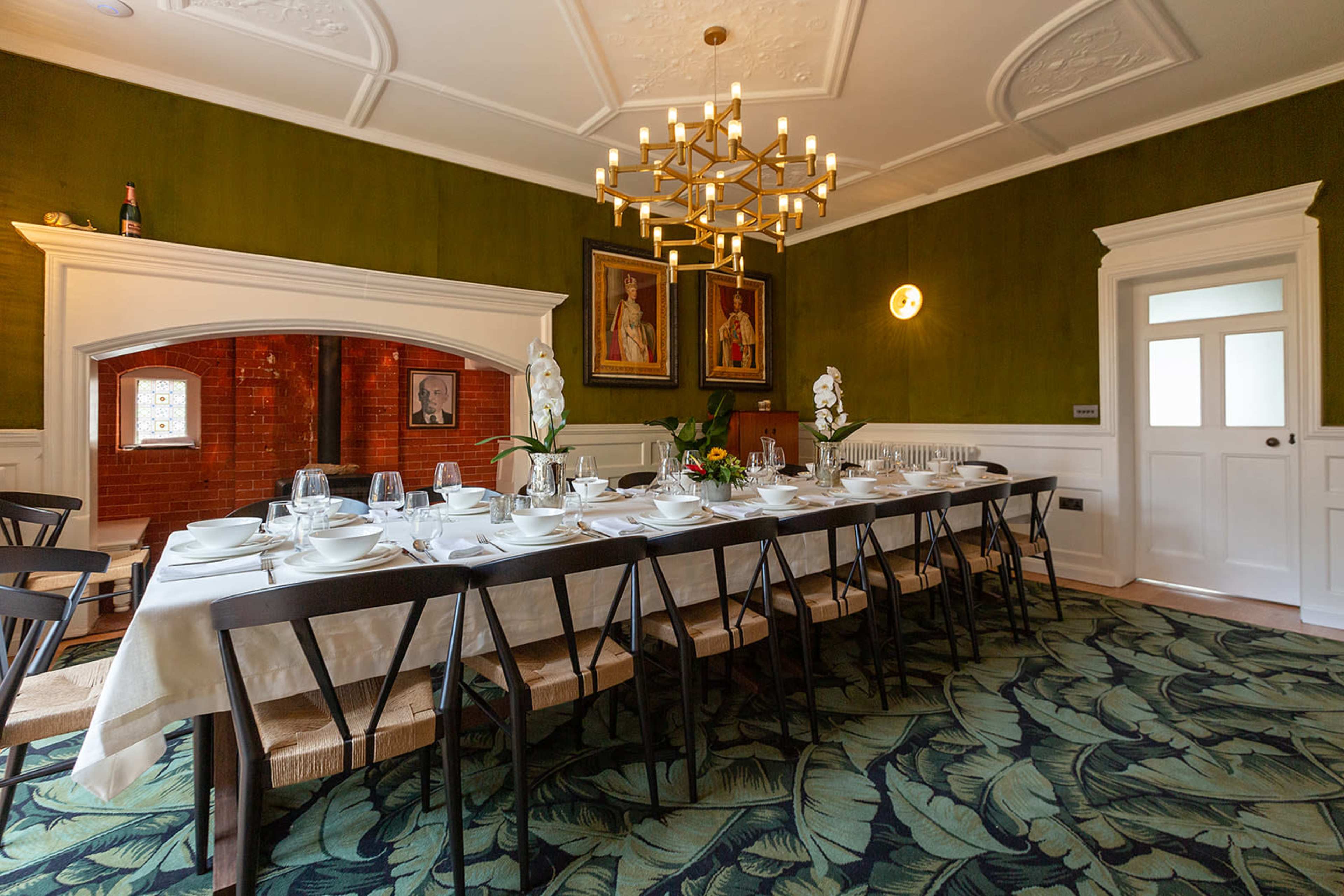 A dining room with a long table set for a meal, surrounded by dark green walls and featuring a chandelier overhead.