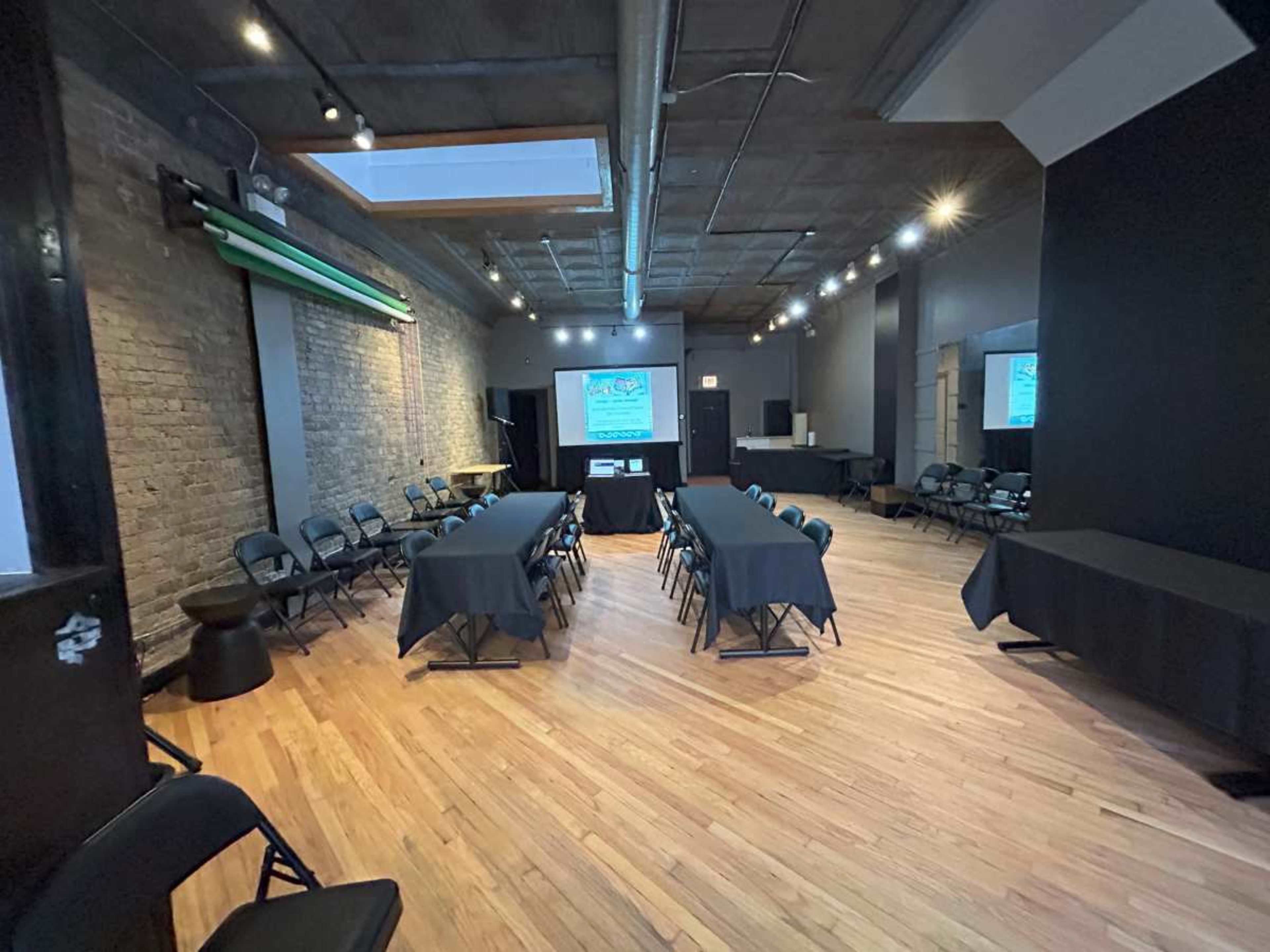 The image shows a spacious conference room set with black tables and chairs, featuring a large screen and a projector at one end.