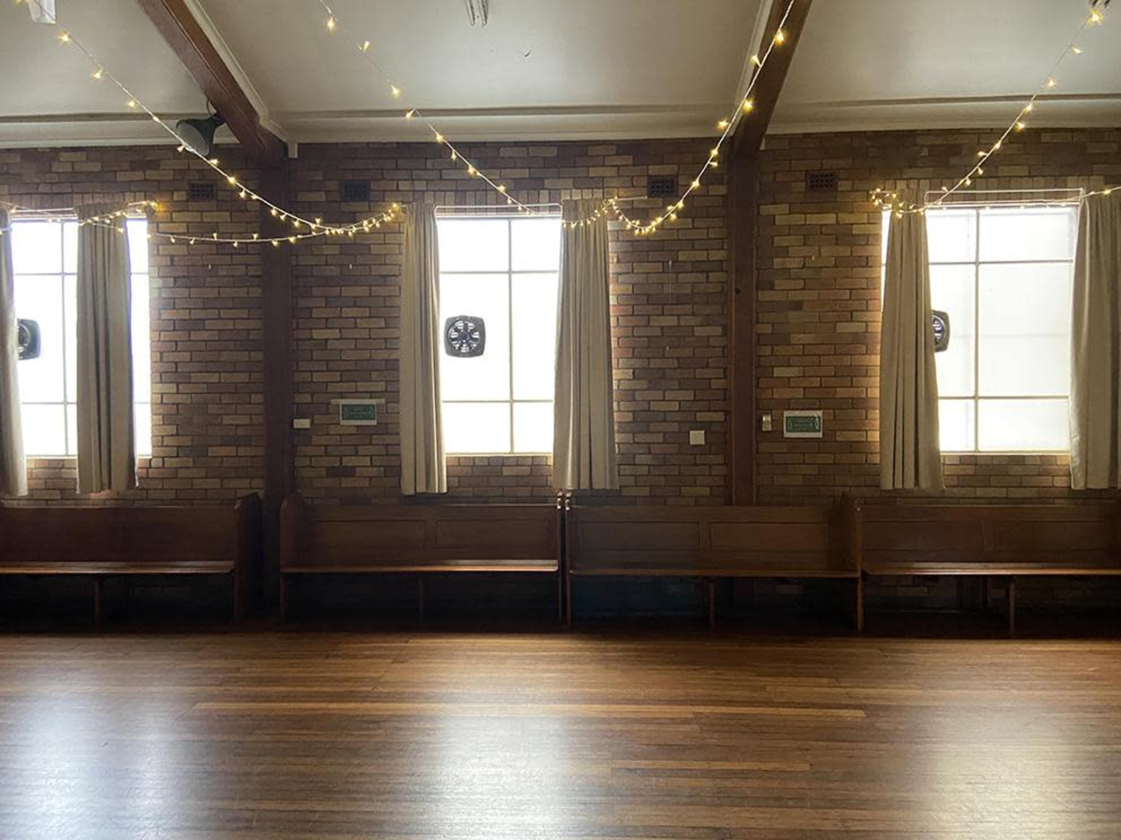 The image shows a room with wooden floors, brick walls, and soft lighting from string lights draped near the windows.